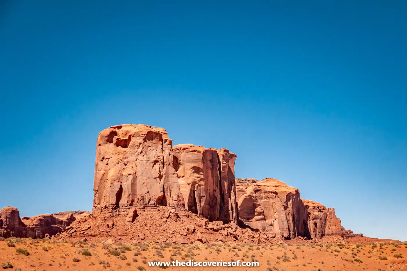 Weathered red sandstone butte rising above scrub and sand on the Monument Valley scenic drive