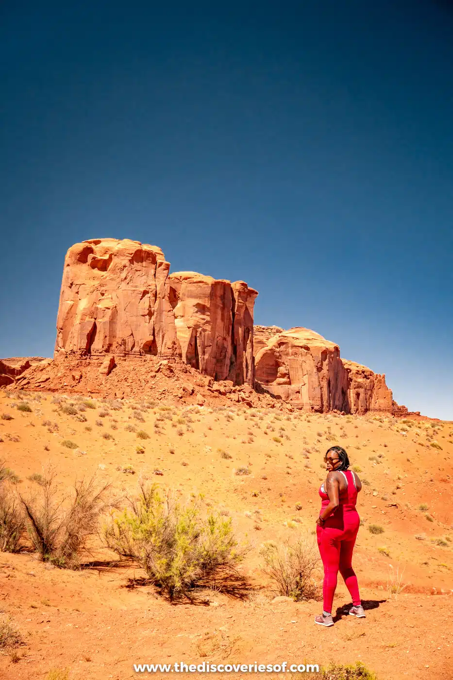 Julianna in a red outfit walking towards a sandstone butte in Monument Valley