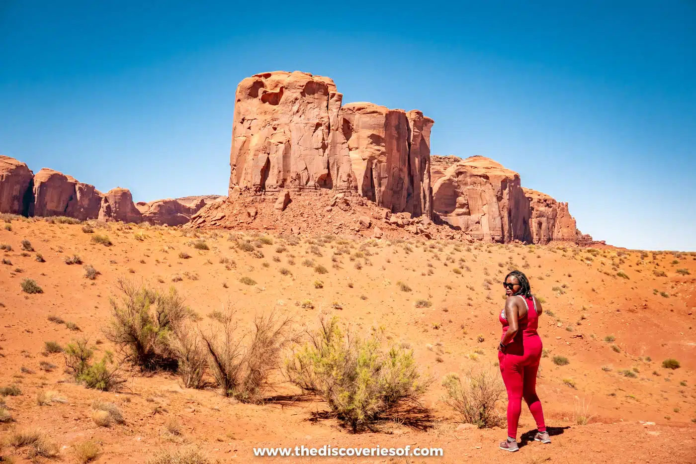 Julianna in red walking across the sand towards a sandstone butte in Monument Valley