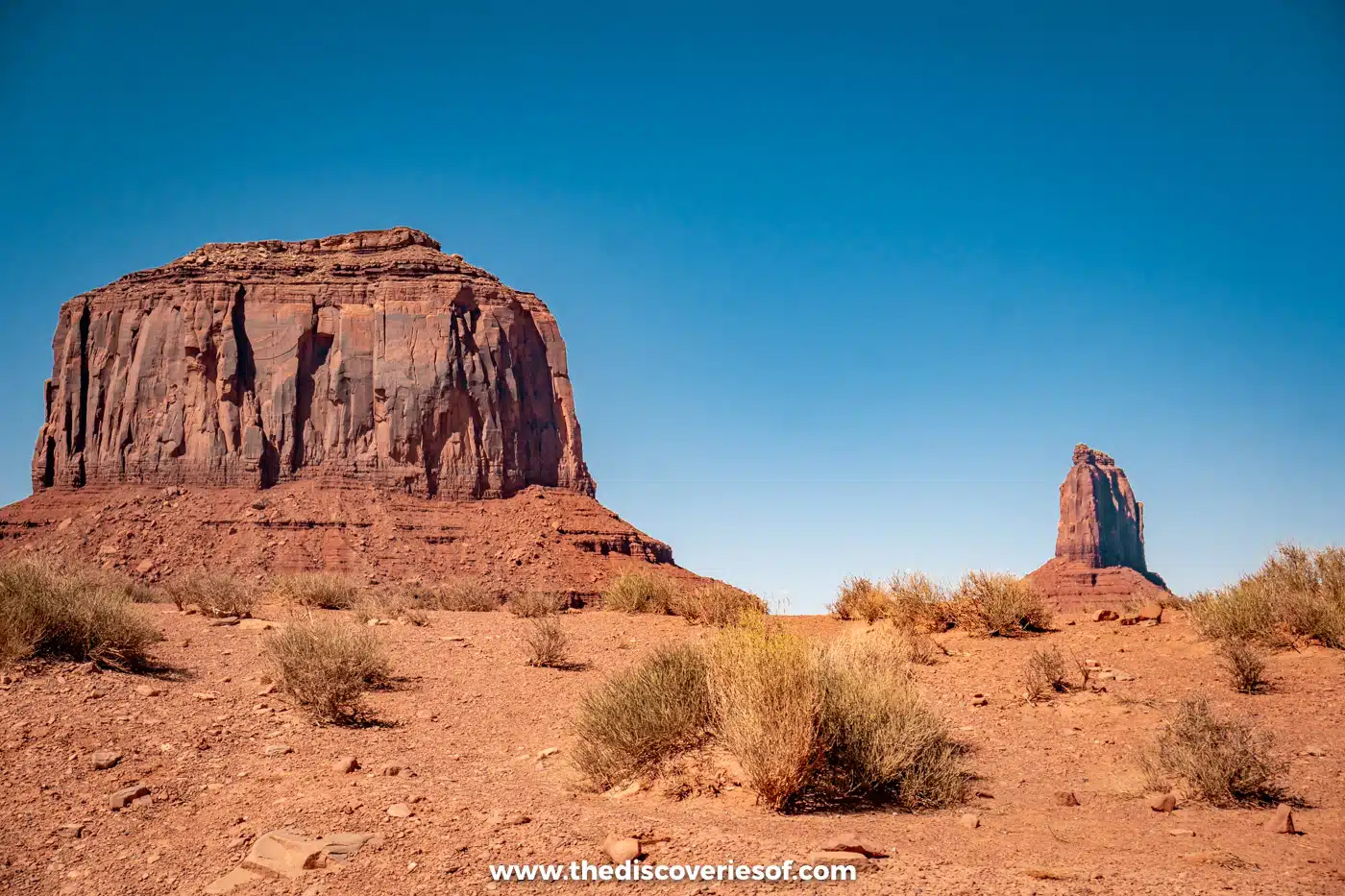 Merrick Butte with the tip of East Mitten beside it, seen across desert scrub in Monument Valley