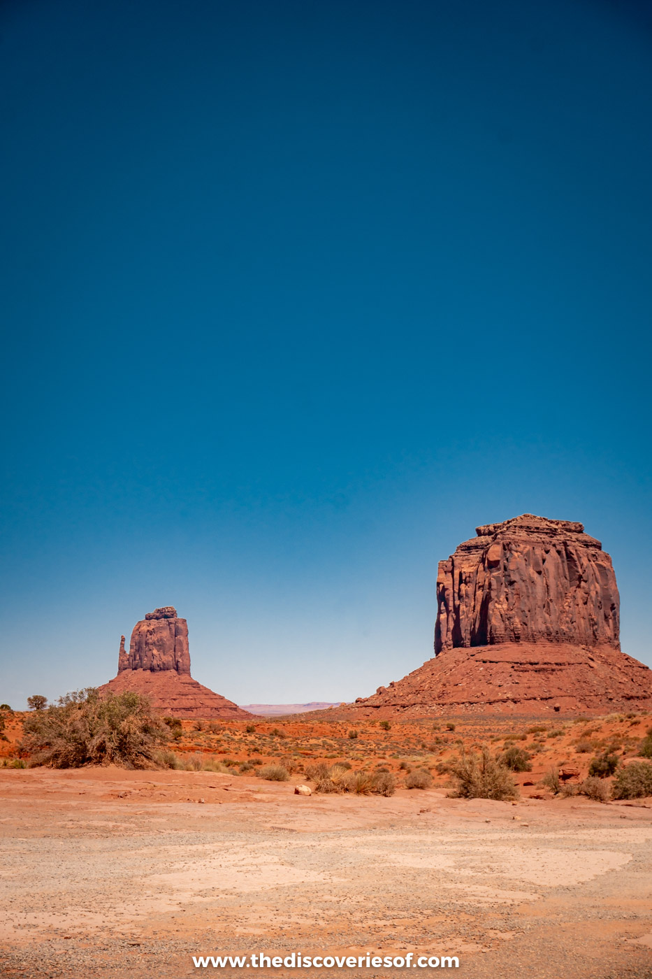 The Mitten buttes rising above a flat sandy clearing in Monument Valley