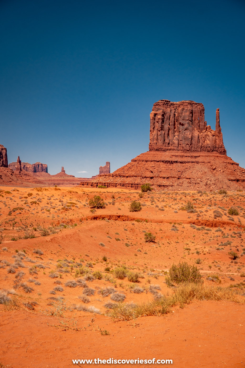 West Mitten Butte rising above red sand and scattered scrub in Monument Valley