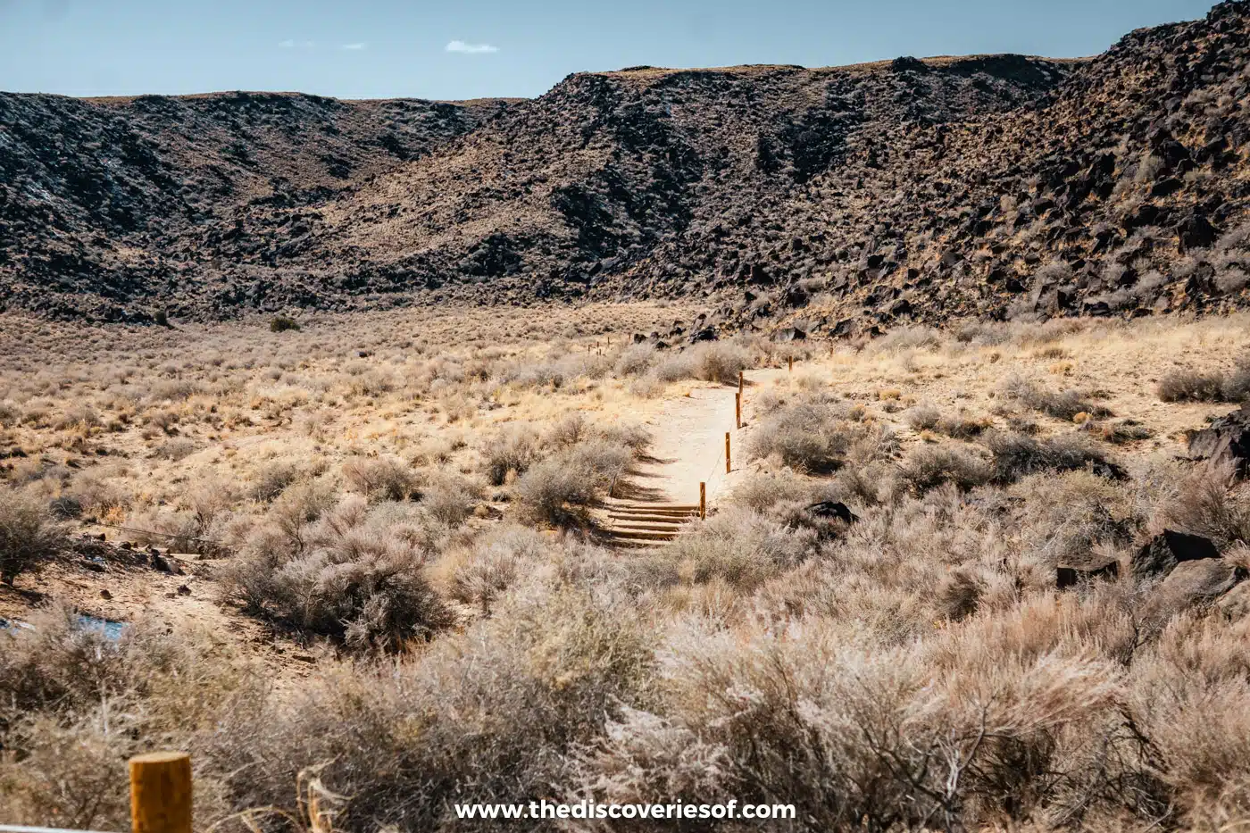 Sandy trail with timber steps leading into Rinconada Canyon below a boulder-strewn volcanic escarpment, Petroglyph National Monument