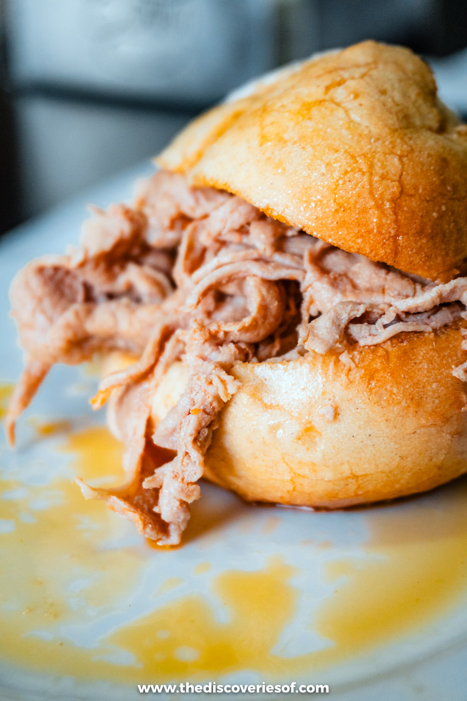 A roast pork sandwich in a soft round bun on a plate at a café in Porto