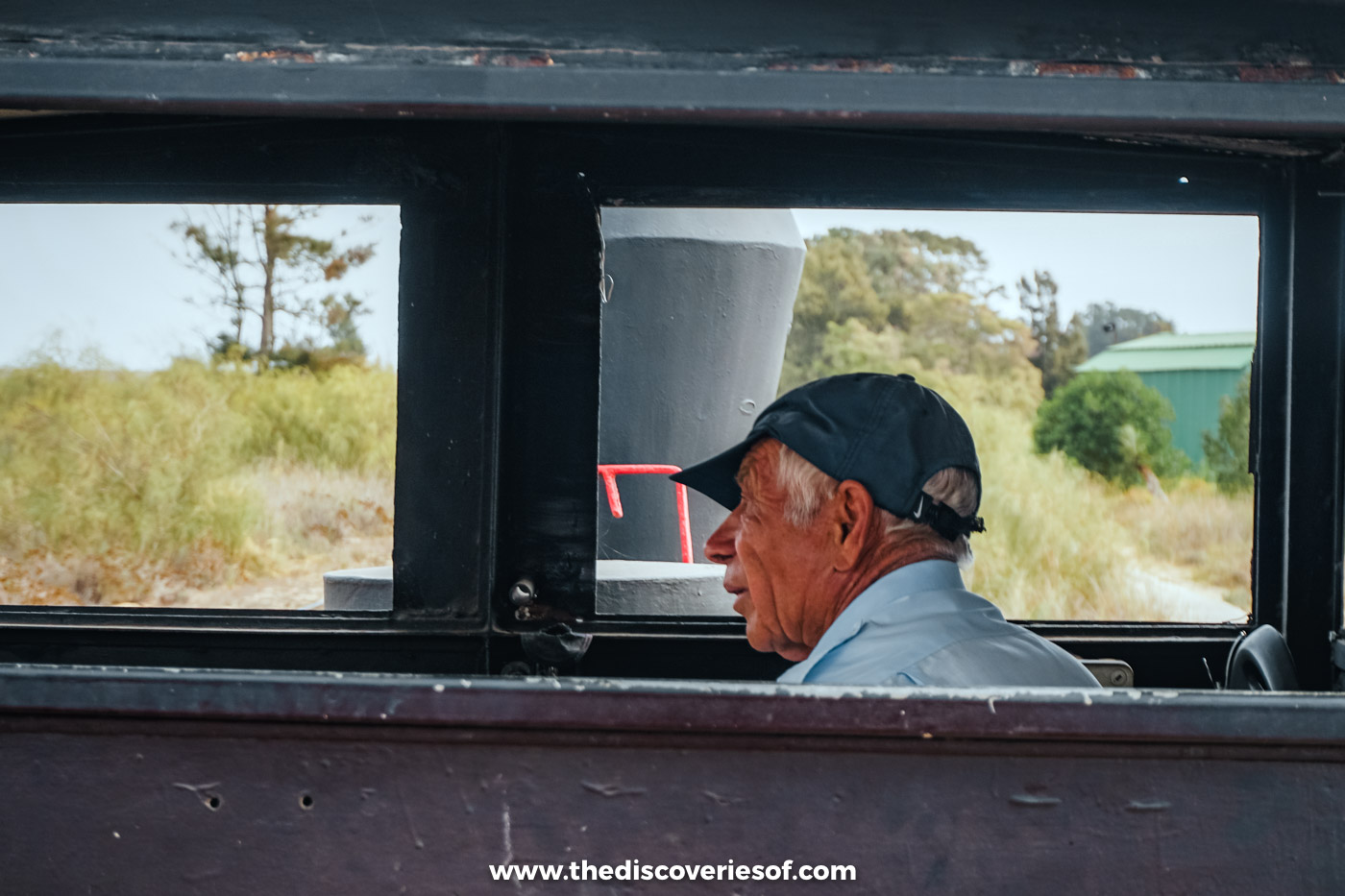 A passenger in a cap seen through the window of a carriage on the little train to Praia do Barril