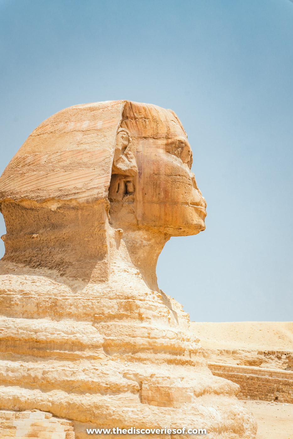 Side view of the weathered limestone head and headdress of the Great Sphinx of Giza against a blue sky
