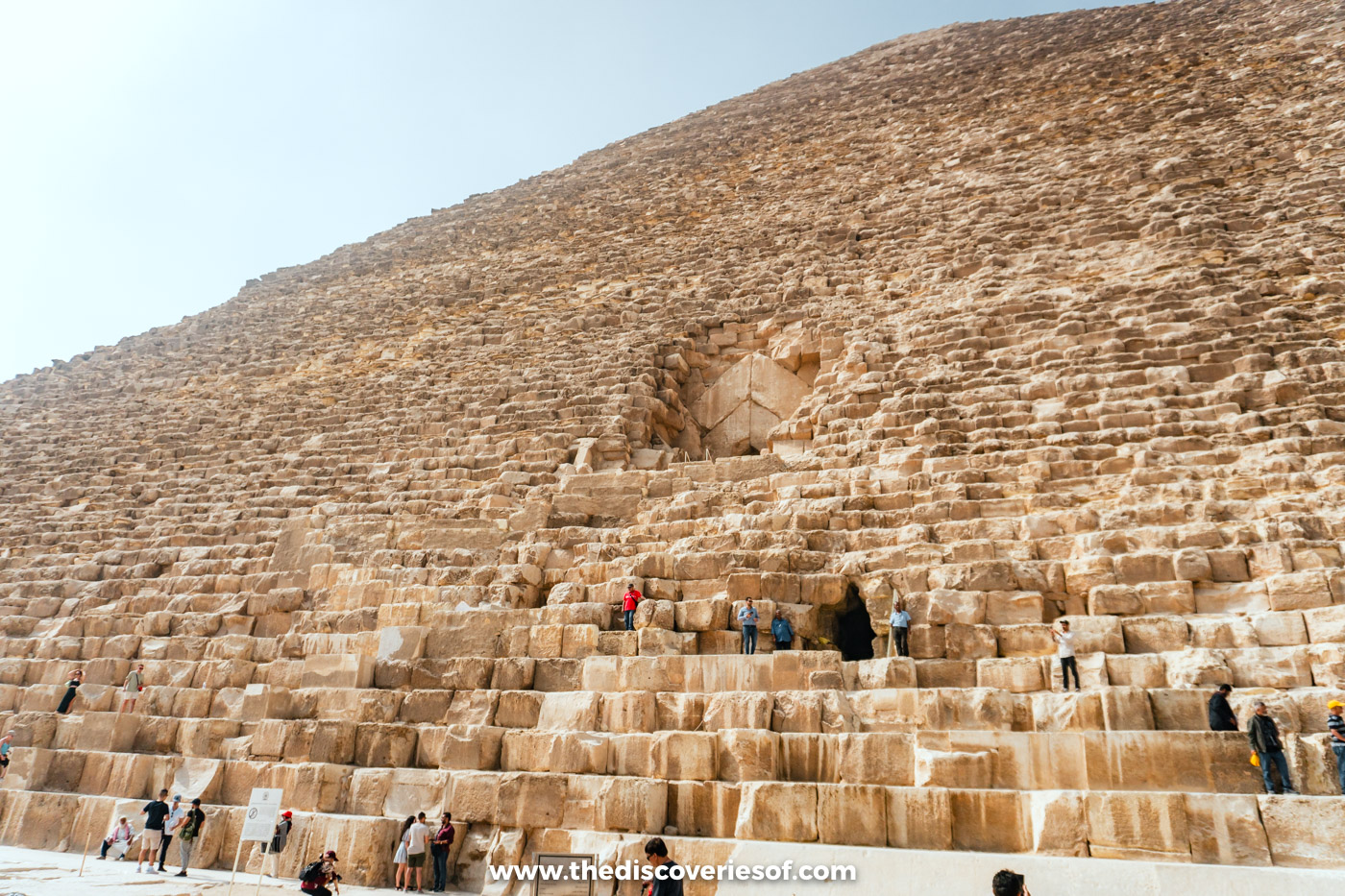 Visitors climbing the lower courses of the Great Pyramid's north face towards the entrance tunnel and the original gabled doorway