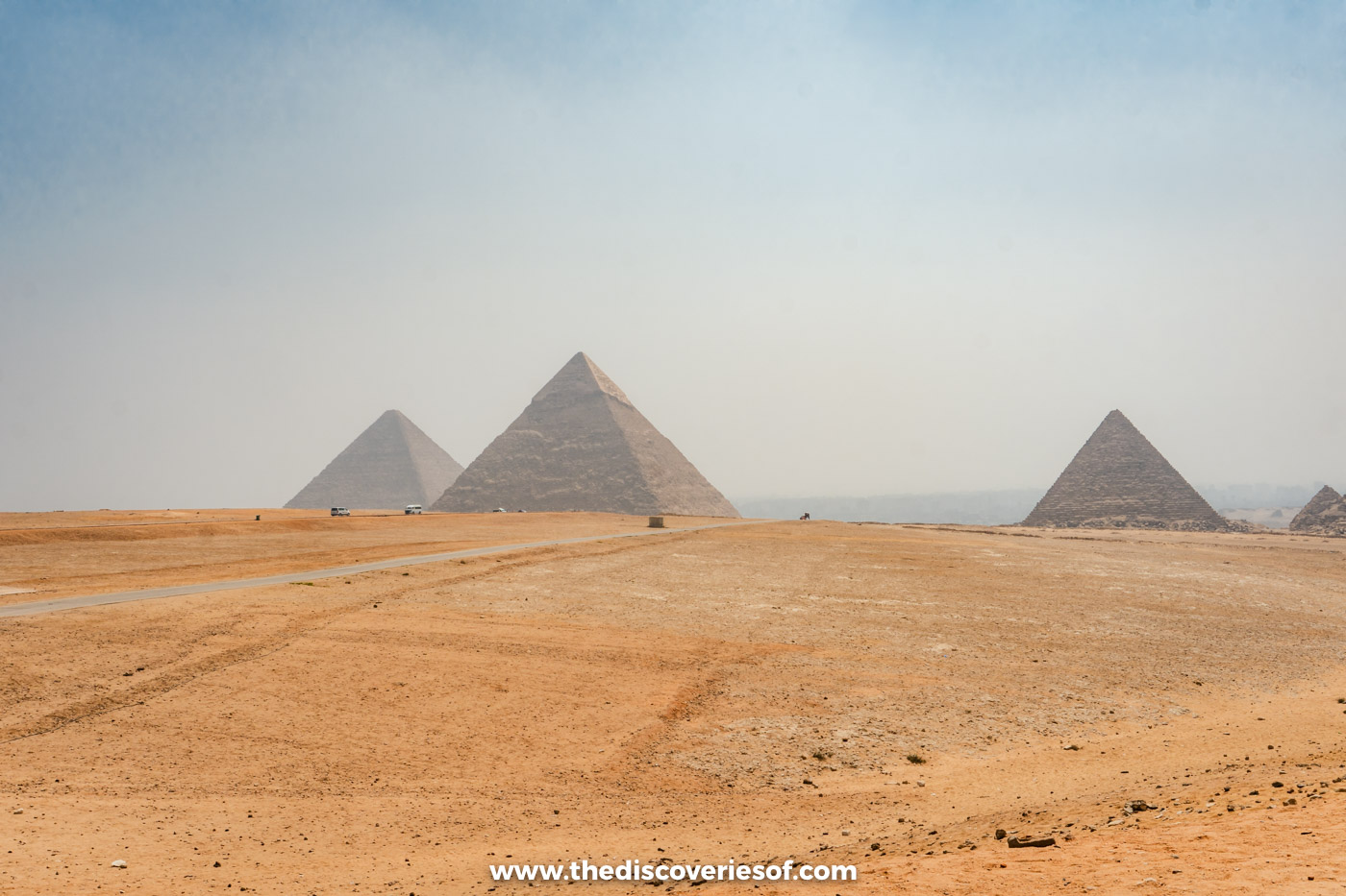 The three Pyramids of Giza in a row across the desert, seen from the panoramic point in the haze