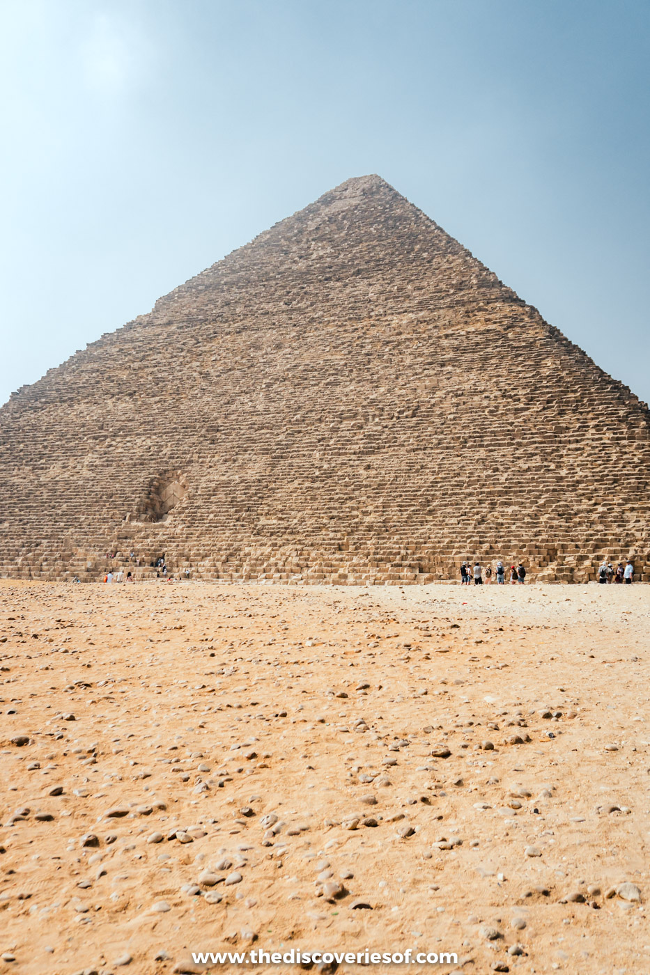 The Great Pyramid of Khufu rising above the sand of the Giza Plateau under a hazy morning sky