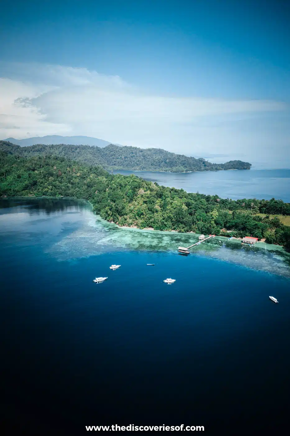 Aerial view of speedboats moored over deep blue water beside the reef, jetty and forest of Birie Island in Raja Ampat