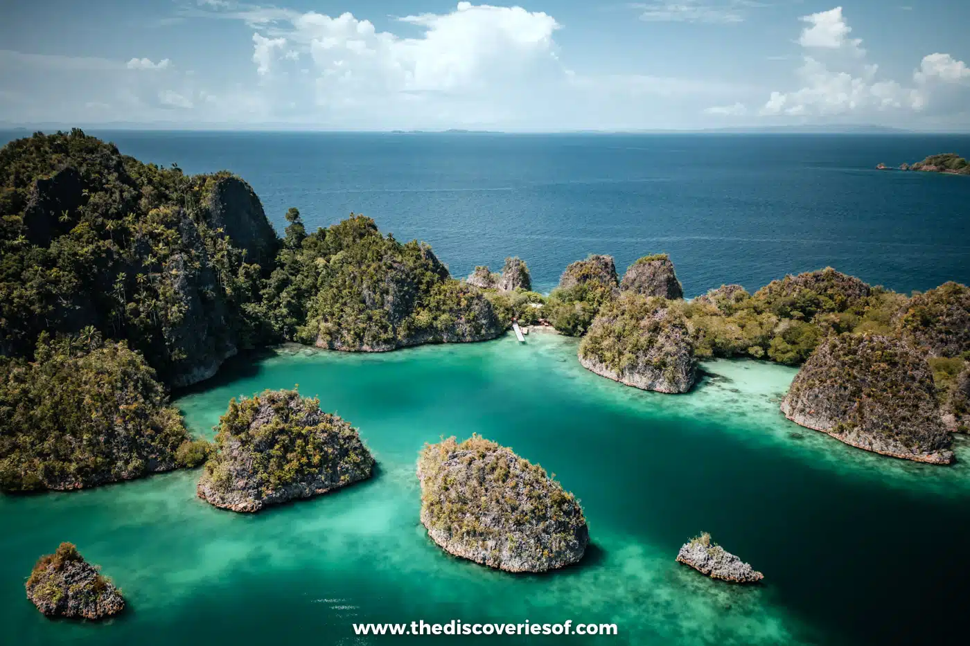 Aerial view of Piaynemo's jungle-topped karst islets scattered across a jade lagoon, with open ocean behind