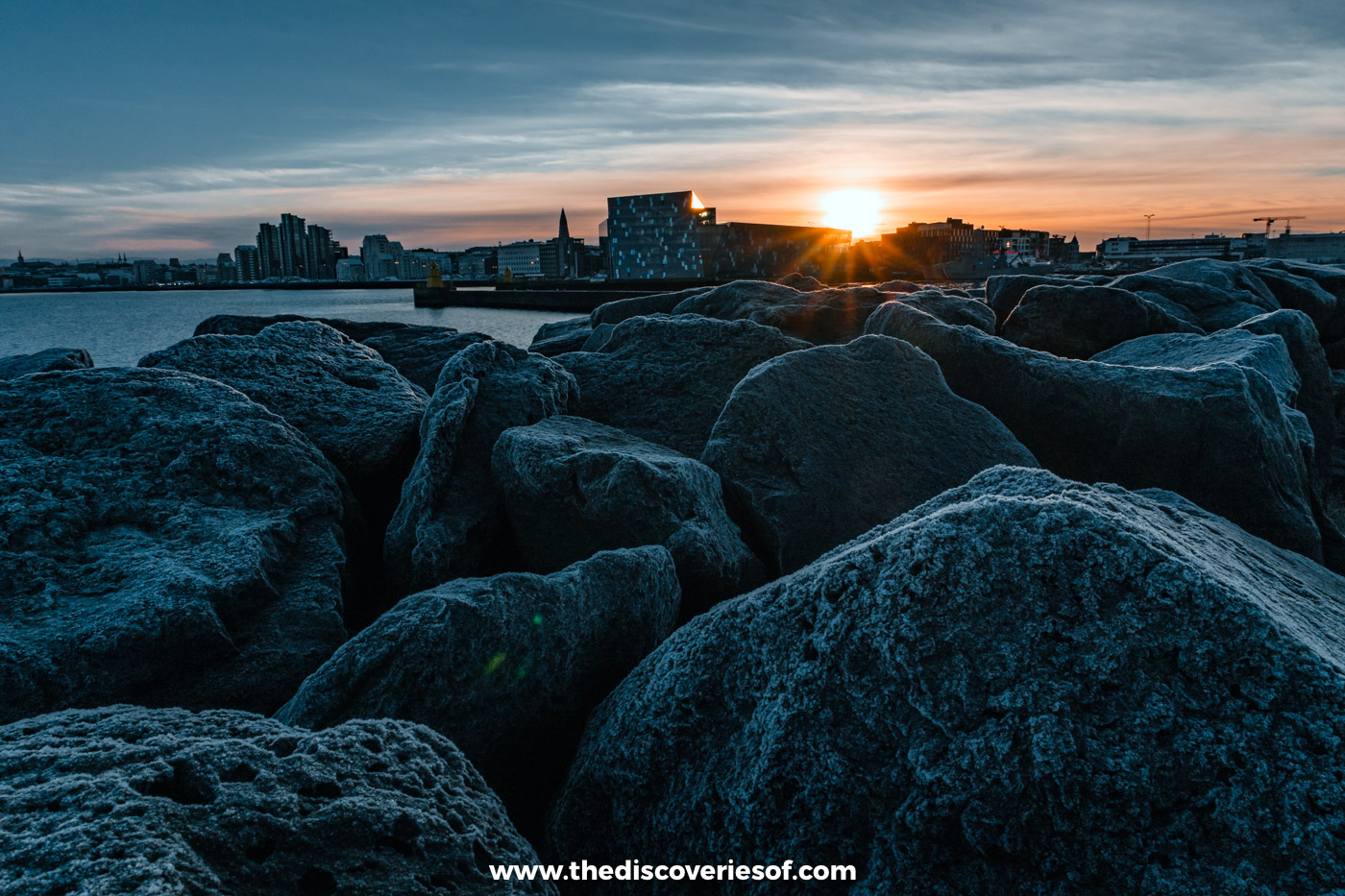 Low December sun setting behind the rooftops of the Reykjavik skyline across the water from Grandi harbour