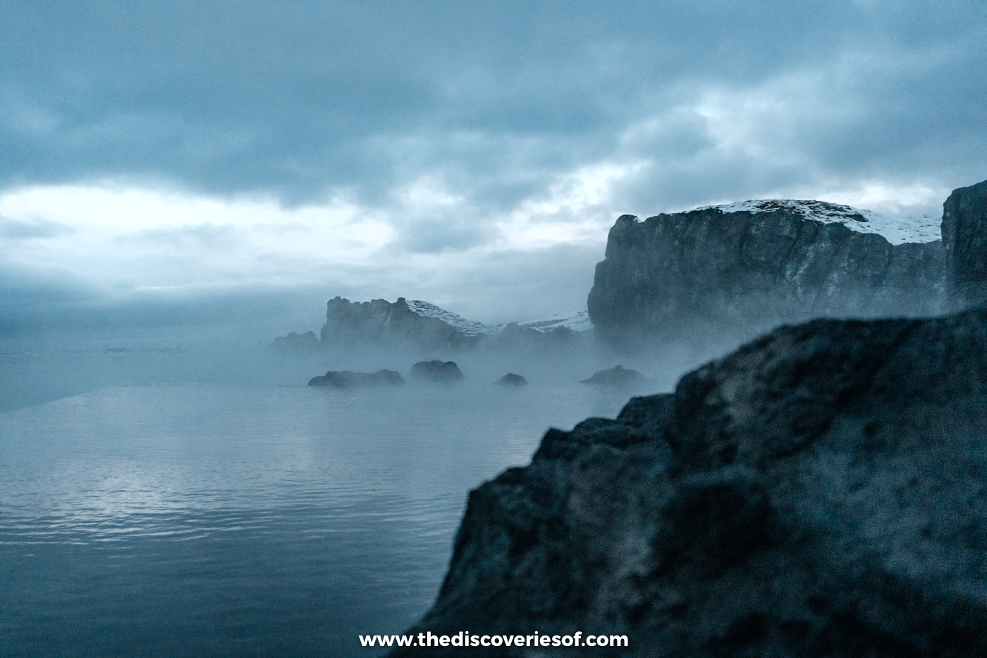 Mist drifting across the warm water and dark lava rocks of Sky Lagoon near Reykjavik in December