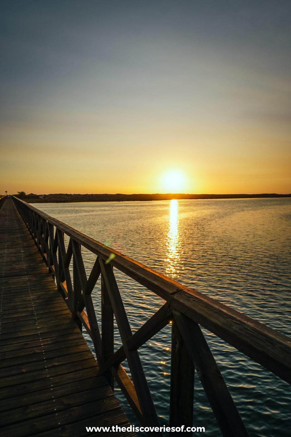 The low evening sun reflecting on the Ria Formosa lagoon beside the wooden railings of the Quinta do Lago footbridge