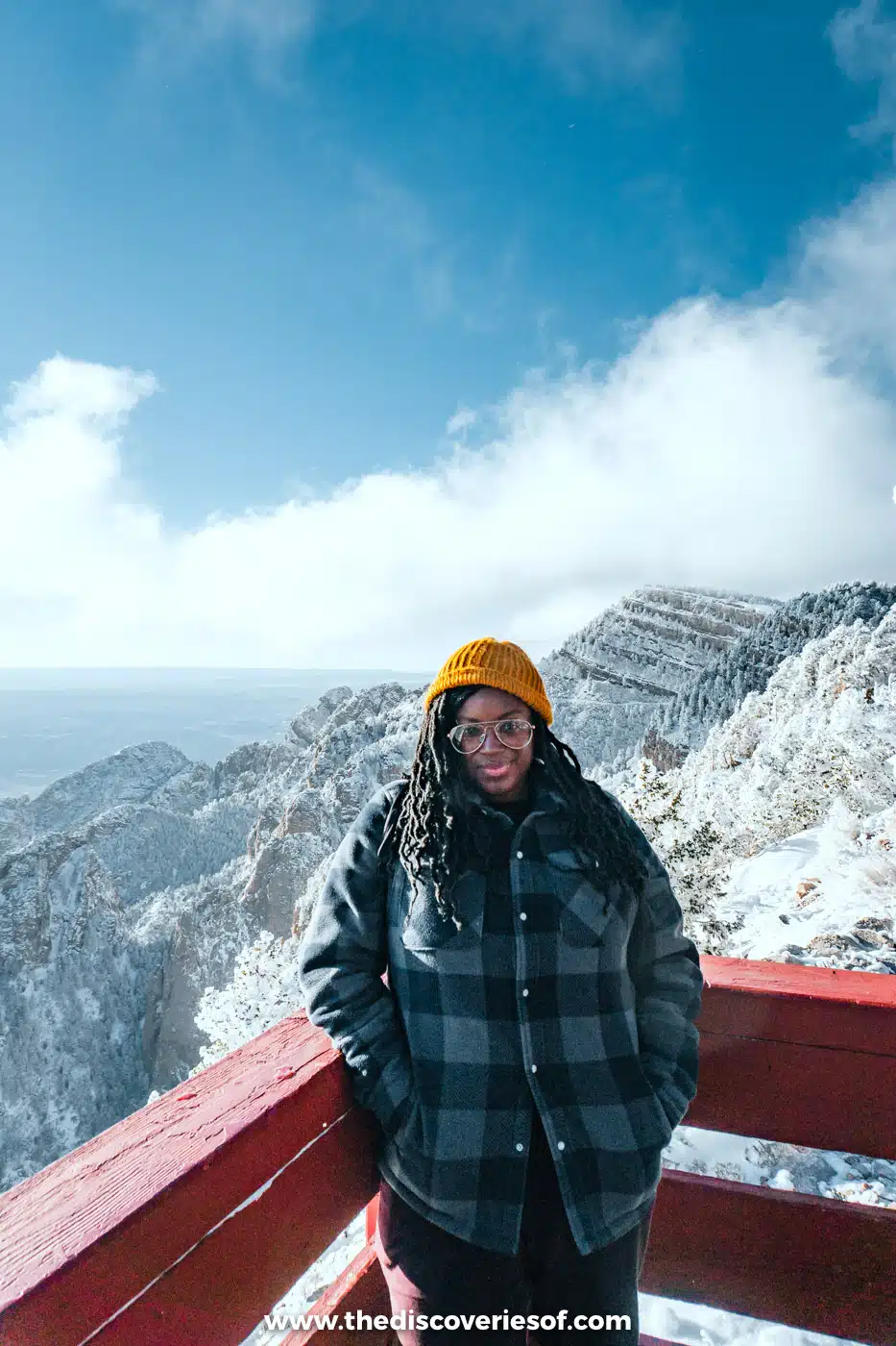 Julianna in a hat and checked coat by the red railing at the top of the Sandia Peak Tramway