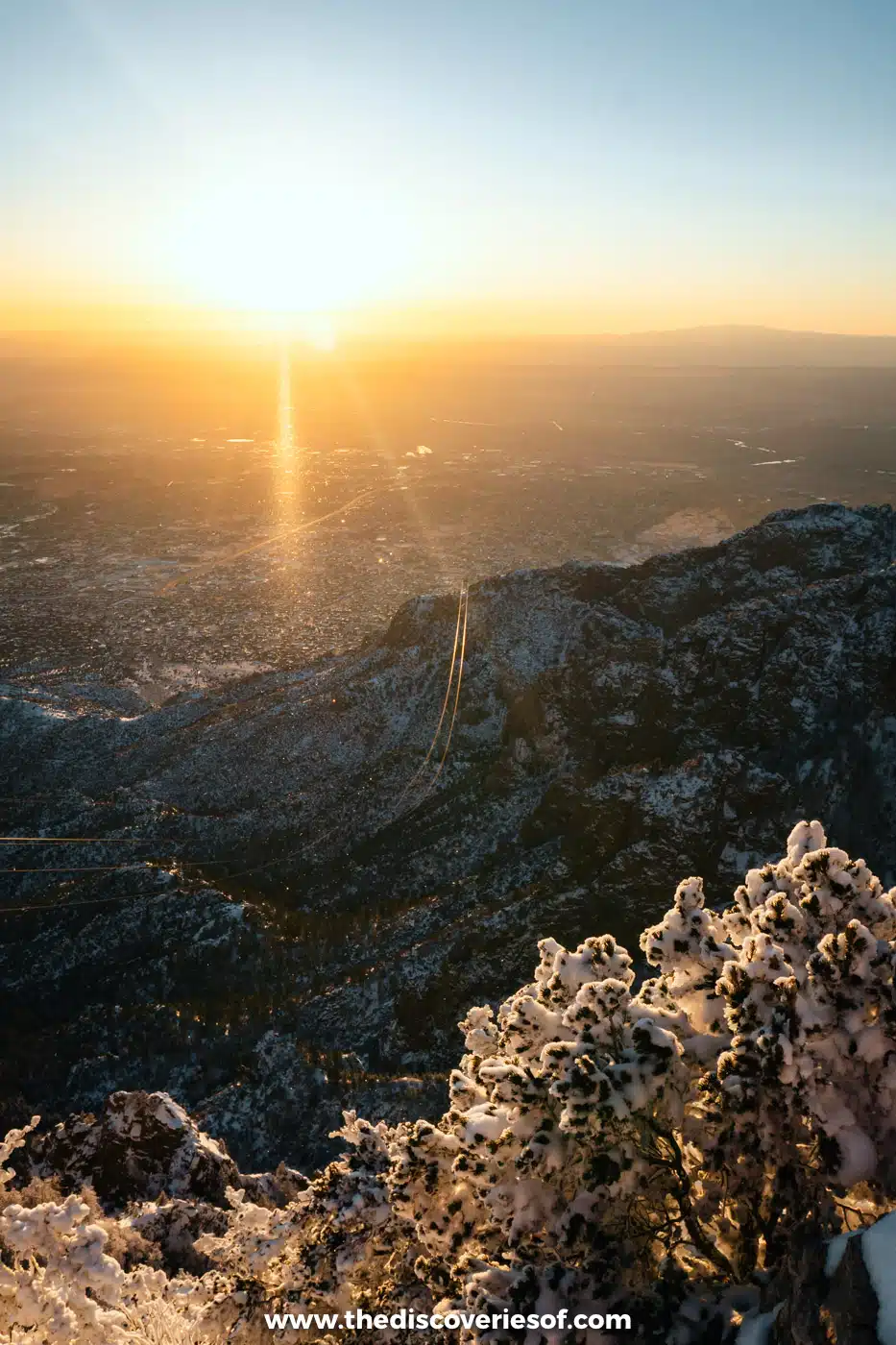 The sun setting over Albuquerque and the desert beyond, seen from the snowy summit of Sandia Peak