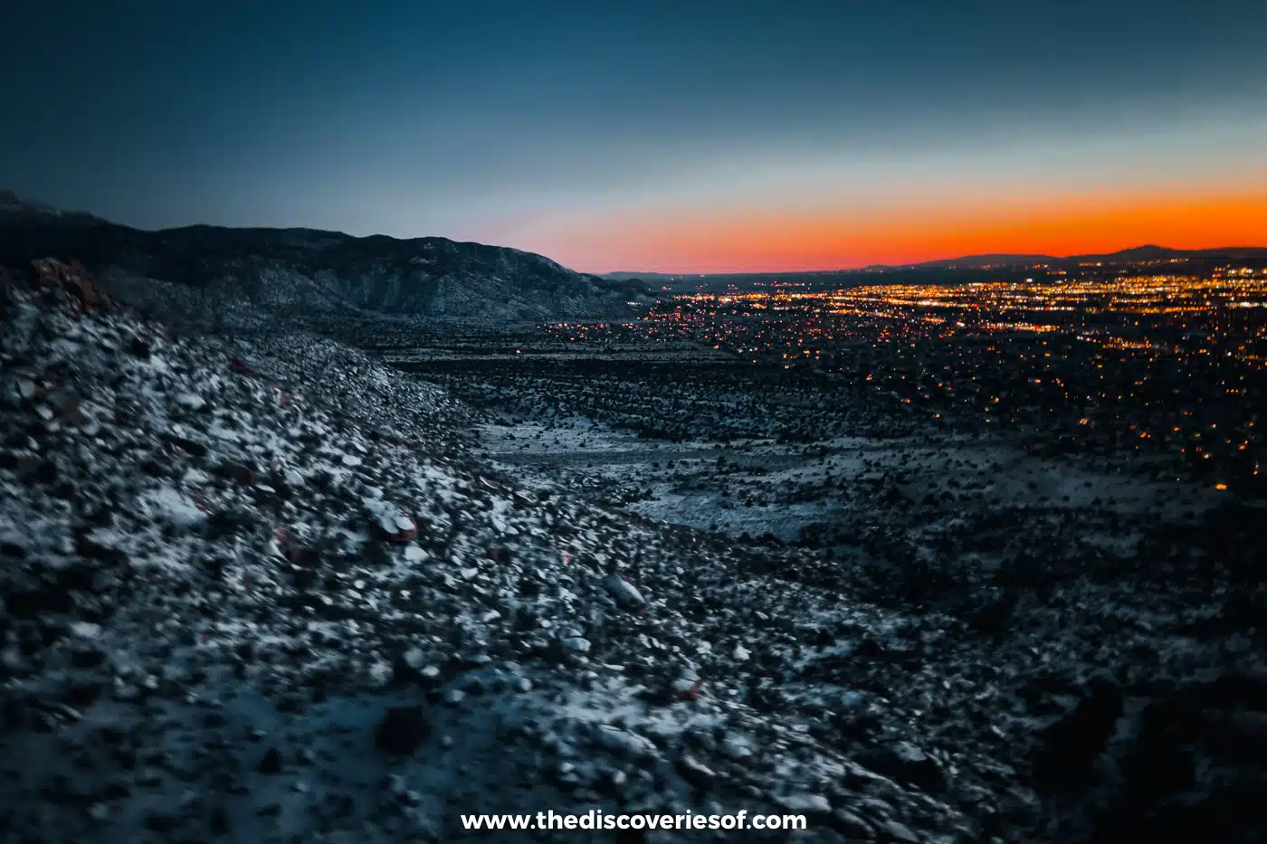 City lights of Albuquerque spread below the dark Sandia Mountains just after sunset