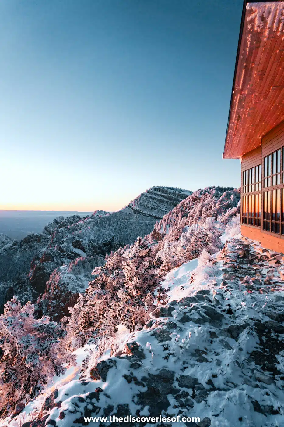 Upper terminal building of the Sandia Peak Tramway lit orange by the setting sun above pink snowy rocks