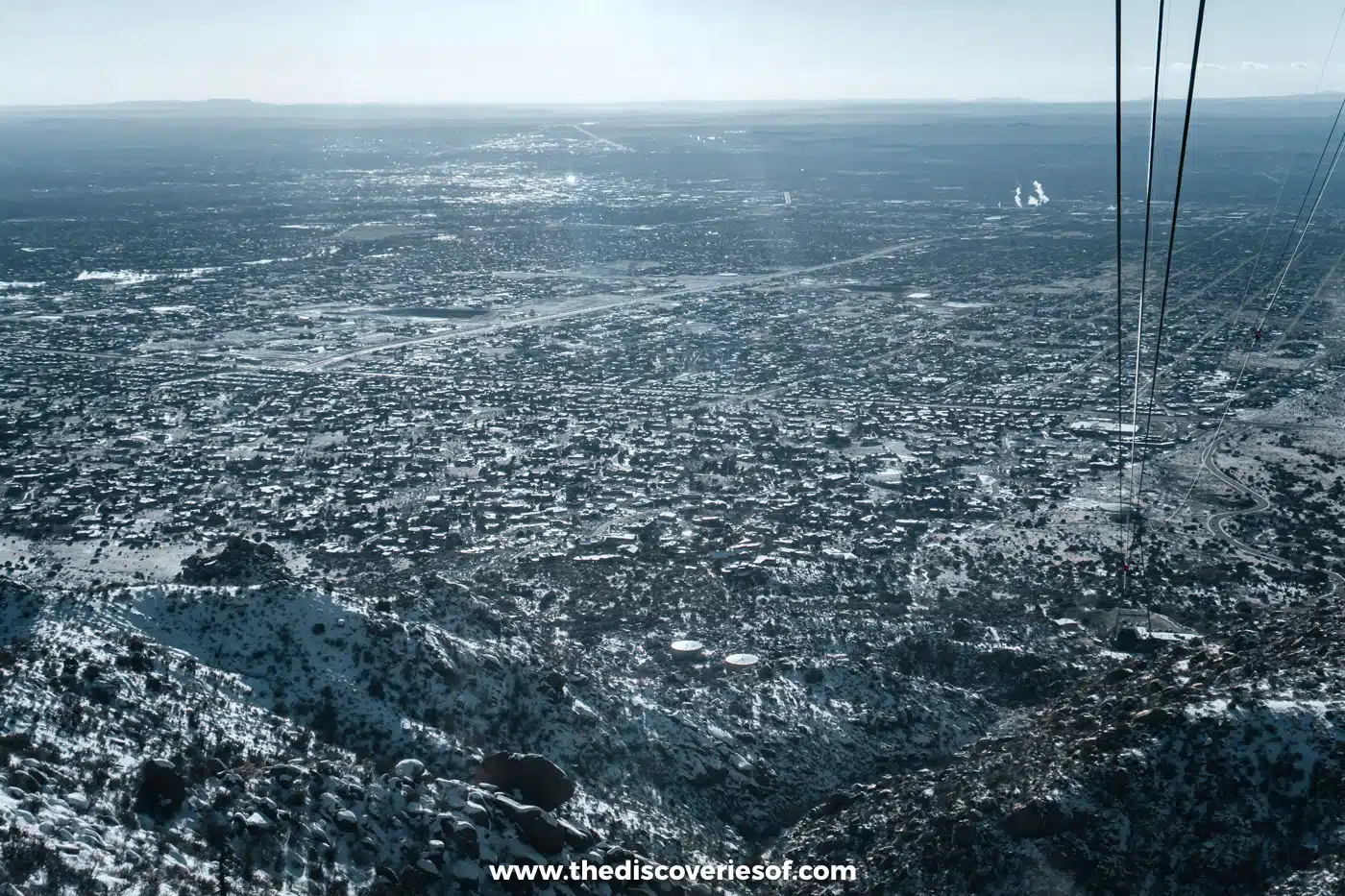 The tram cables running down over snowy slopes towards the spread-out city of Albuquerque below Sandia Peak