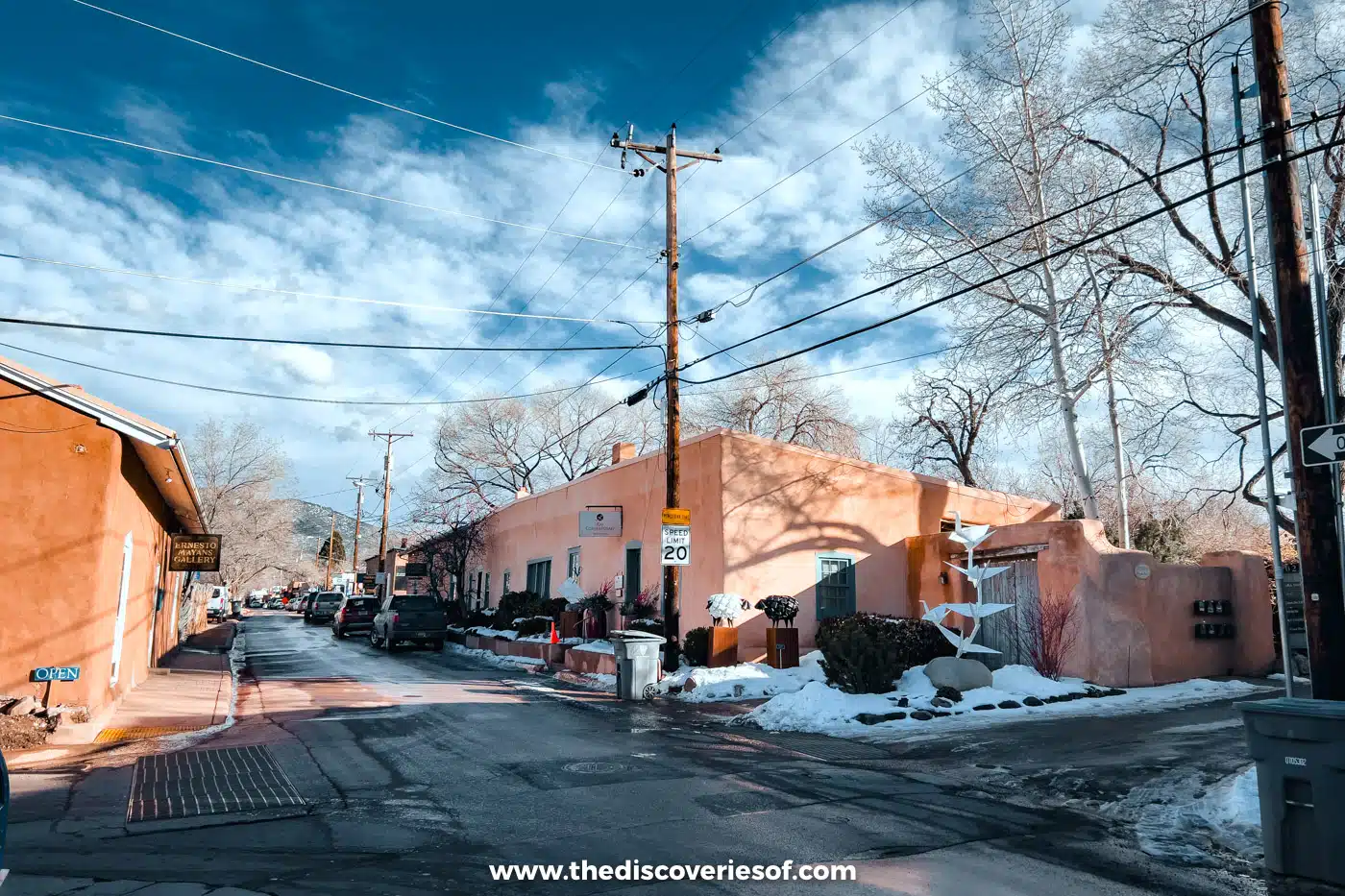 Snow-edged street lined with adobe galleries and bare trees on Canyon Road in Santa Fe in winter