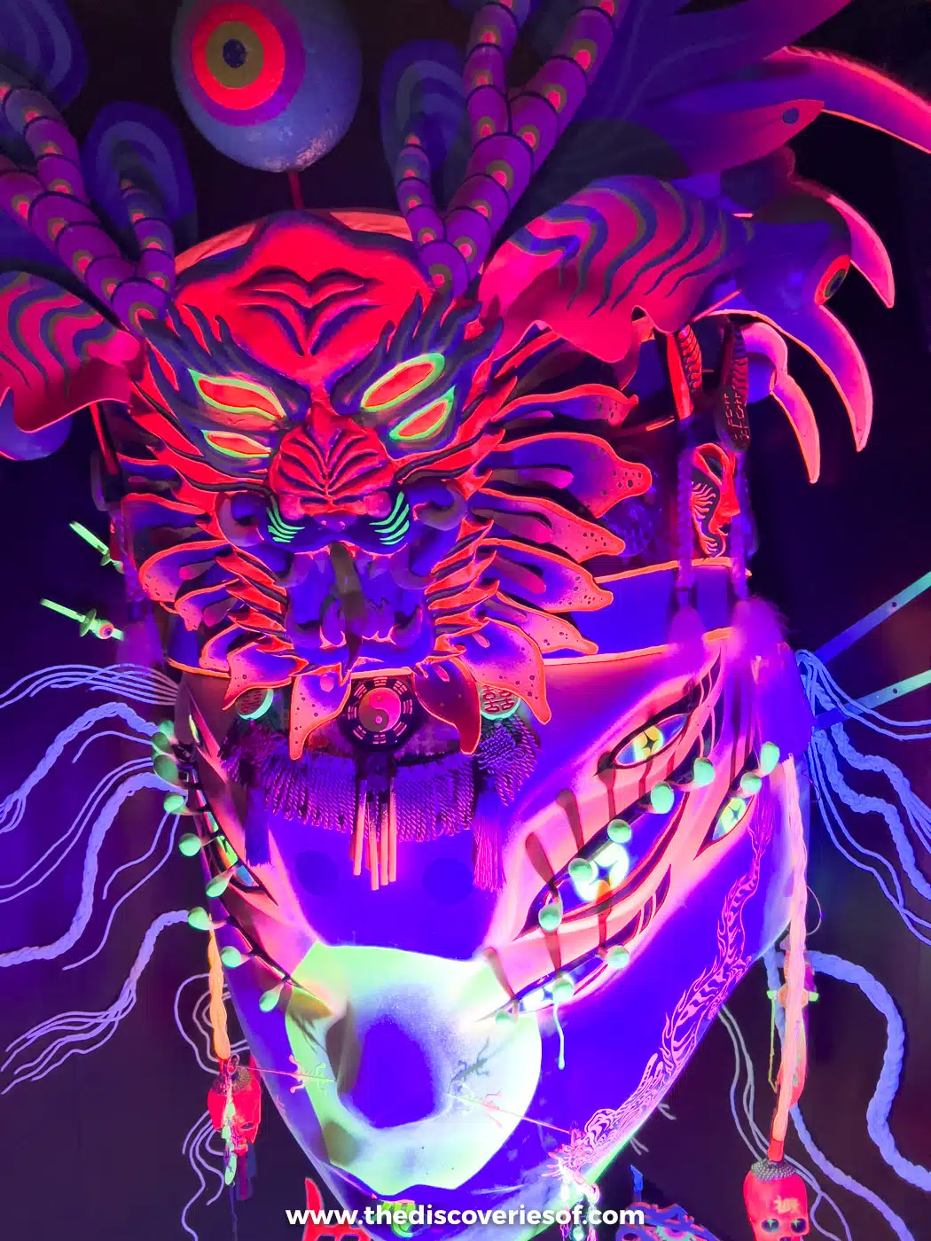 Giant glowing mask in red, purple and blue under ultraviolet light inside Meow Wolf's House of Eternal Return