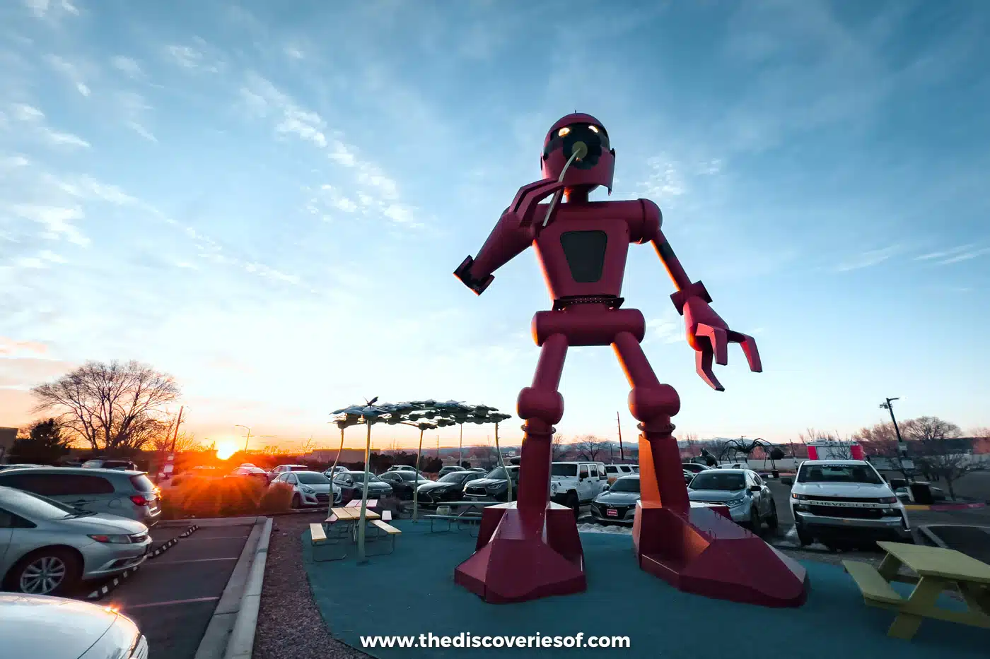 Giant red robot sculpture outside Meow Wolf in Santa Fe at sunset, with the car park behind