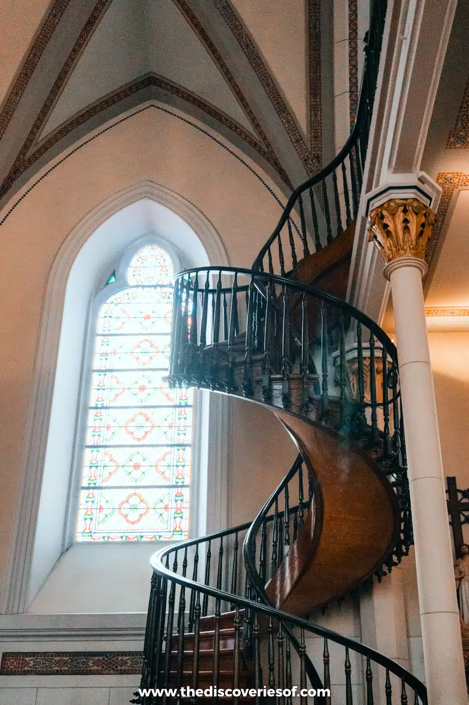 Wooden spiral staircase curving up to the choir loft beside a stained glass window in Loretto Chapel, Santa Fe