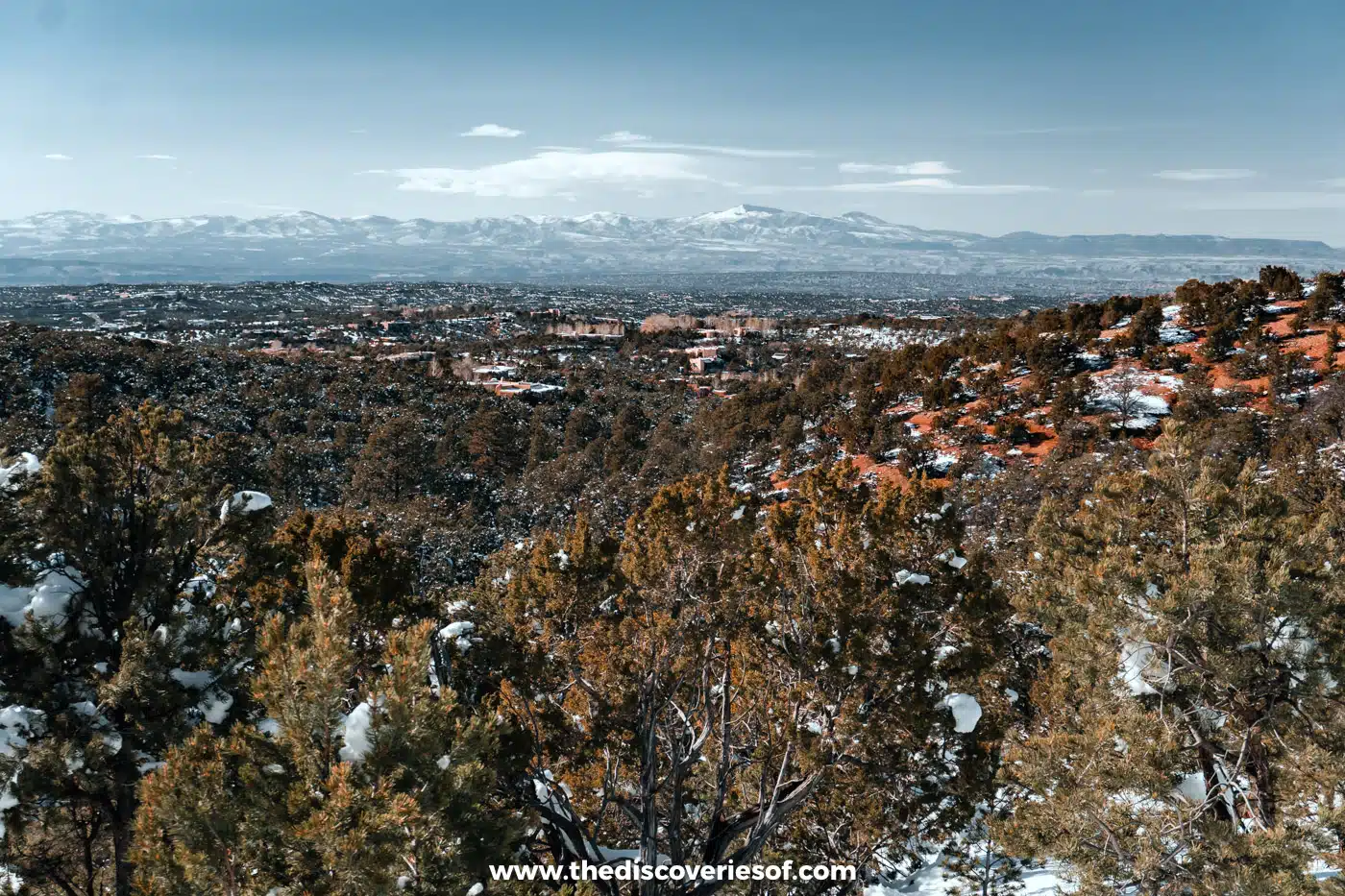 View over Santa Fe from the snowy juniper-covered foothills towards distant snow-capped mountains in February
