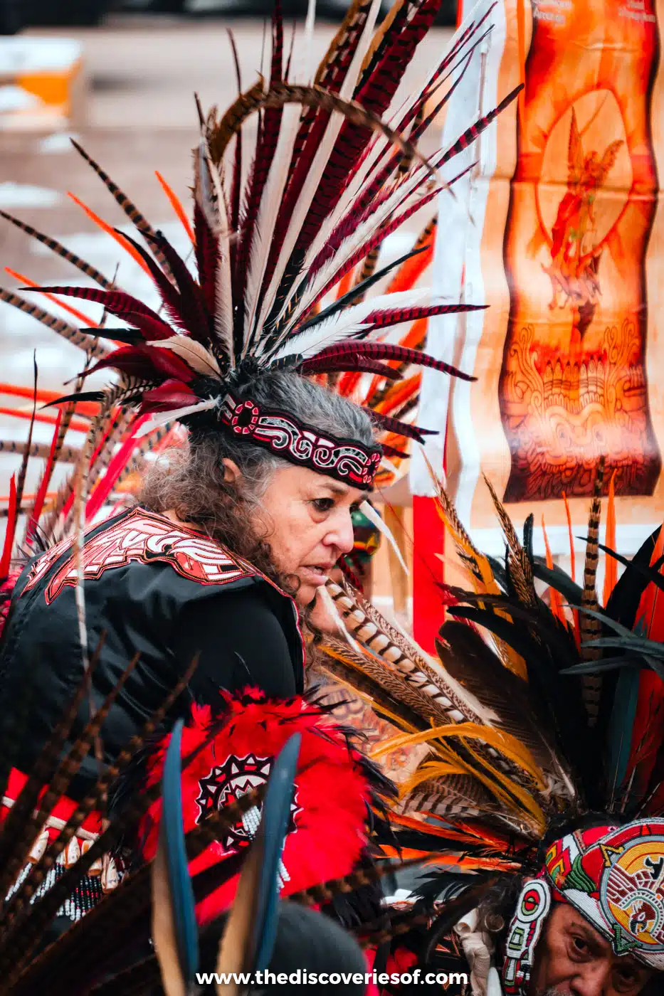 Dancer in a tall feathered headdress and red and black regalia at a Native American gathering on Taos Plaza