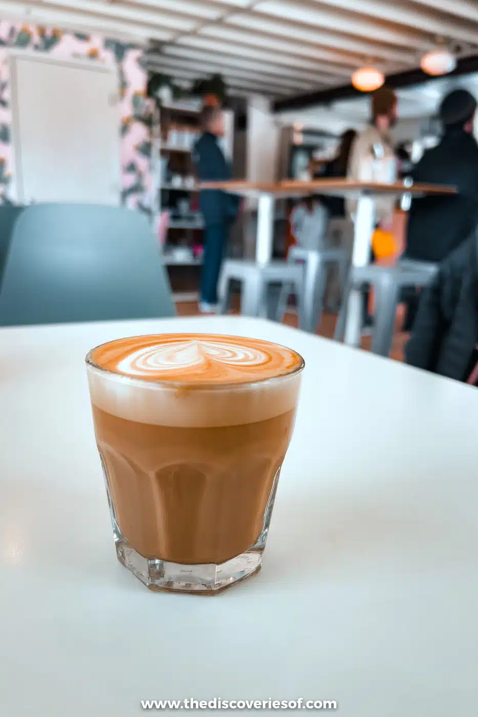 Cortado with latte art in a glass on a white table at the Coffee Apothecary cafe in Taos