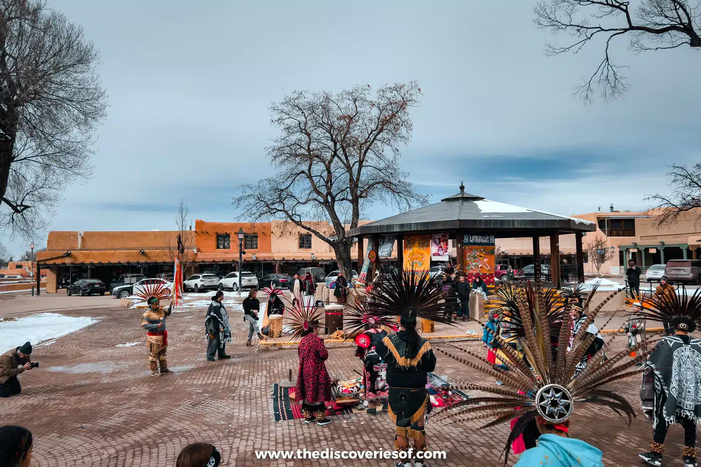 Dancers in feathered headdresses at a Native American gathering on snowy Taos Plaza beside the bandstand