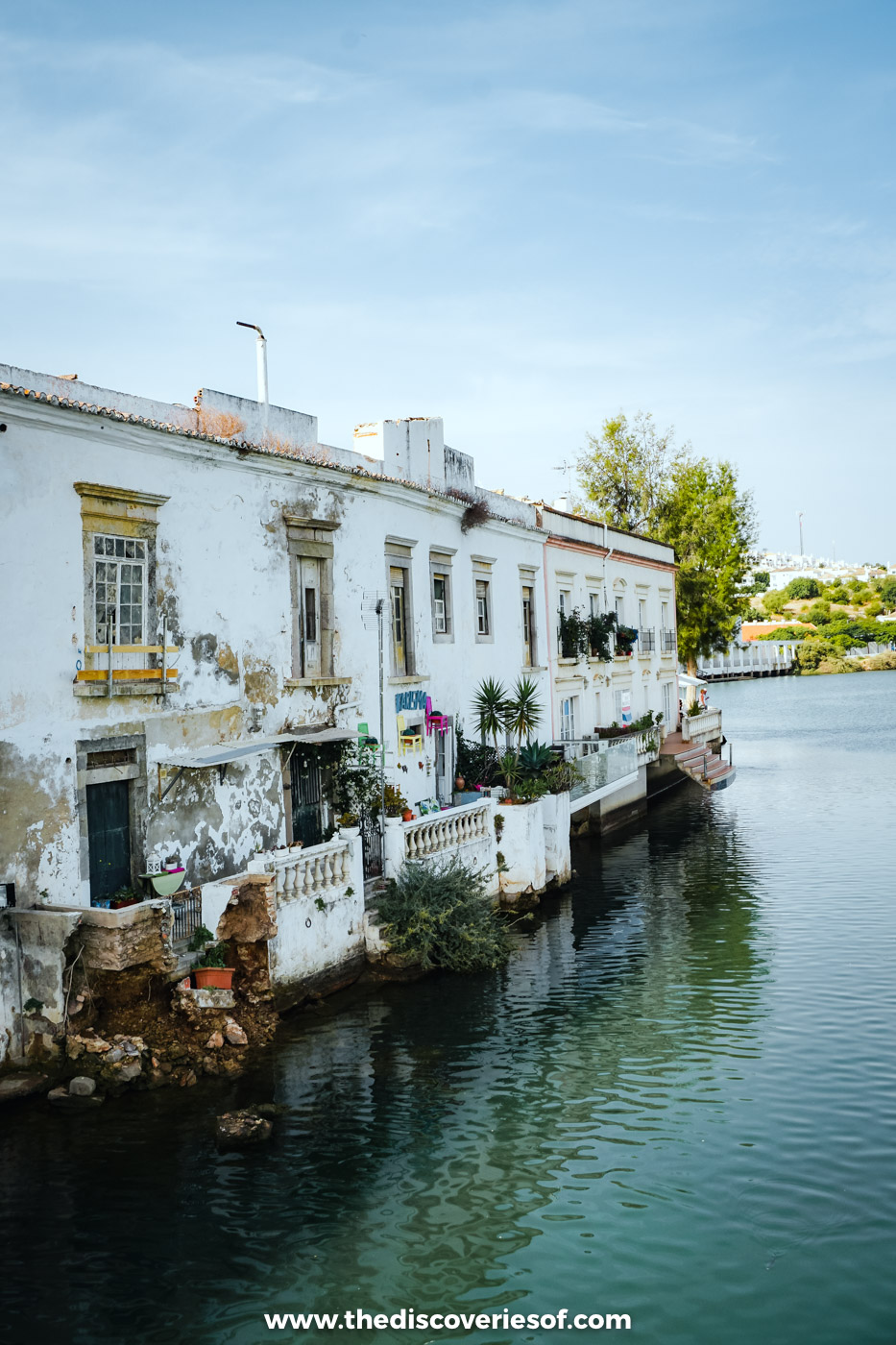 Old whitewashed houses with balconies lining the calm Rio Gilão in Tavira under a pale blue sky