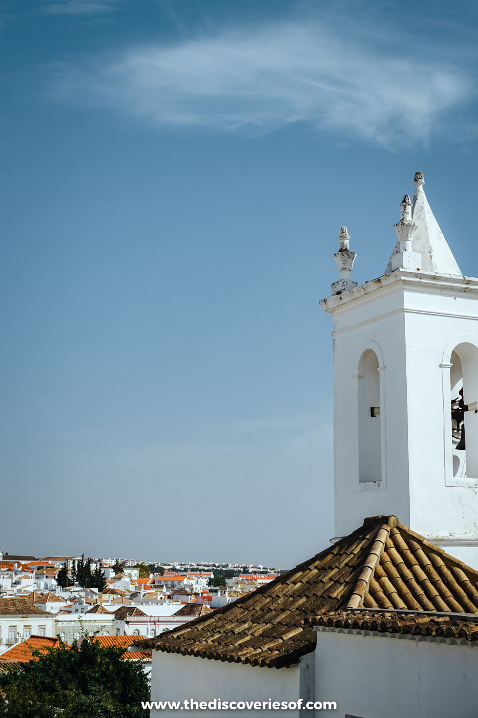 A whitewashed church bell tower and tiled roof above the rooftops of Tavira under a blue sky