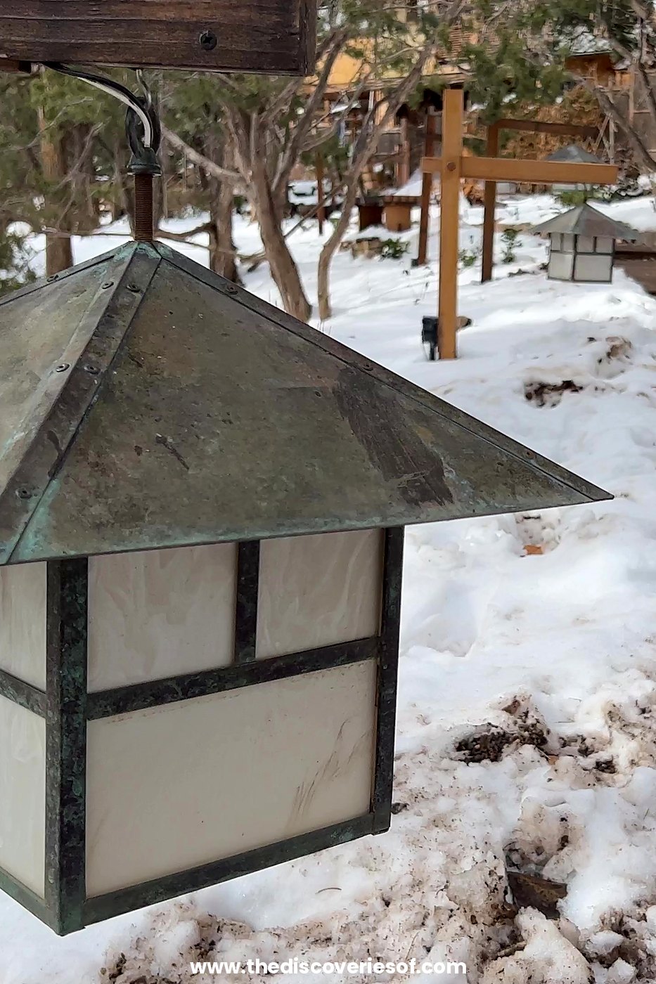 Copper lantern hanging above snow beside a pine-lined path at Ten Thousand Waves, Santa Fe