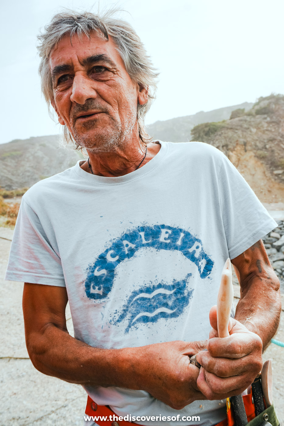 A grey-haired fisherman in a white T-shirt standing by the harbour at Azenha do Mar on the Alentejo coast