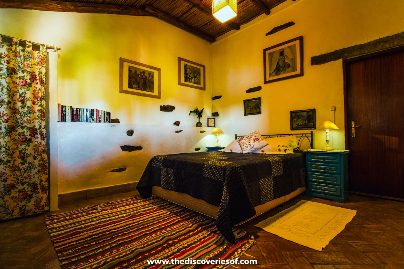 A double bed with a dark patchwork bedspread, a striped rug and framed pictures on yellow walls in a room at Quinta do Barranco da Estrada