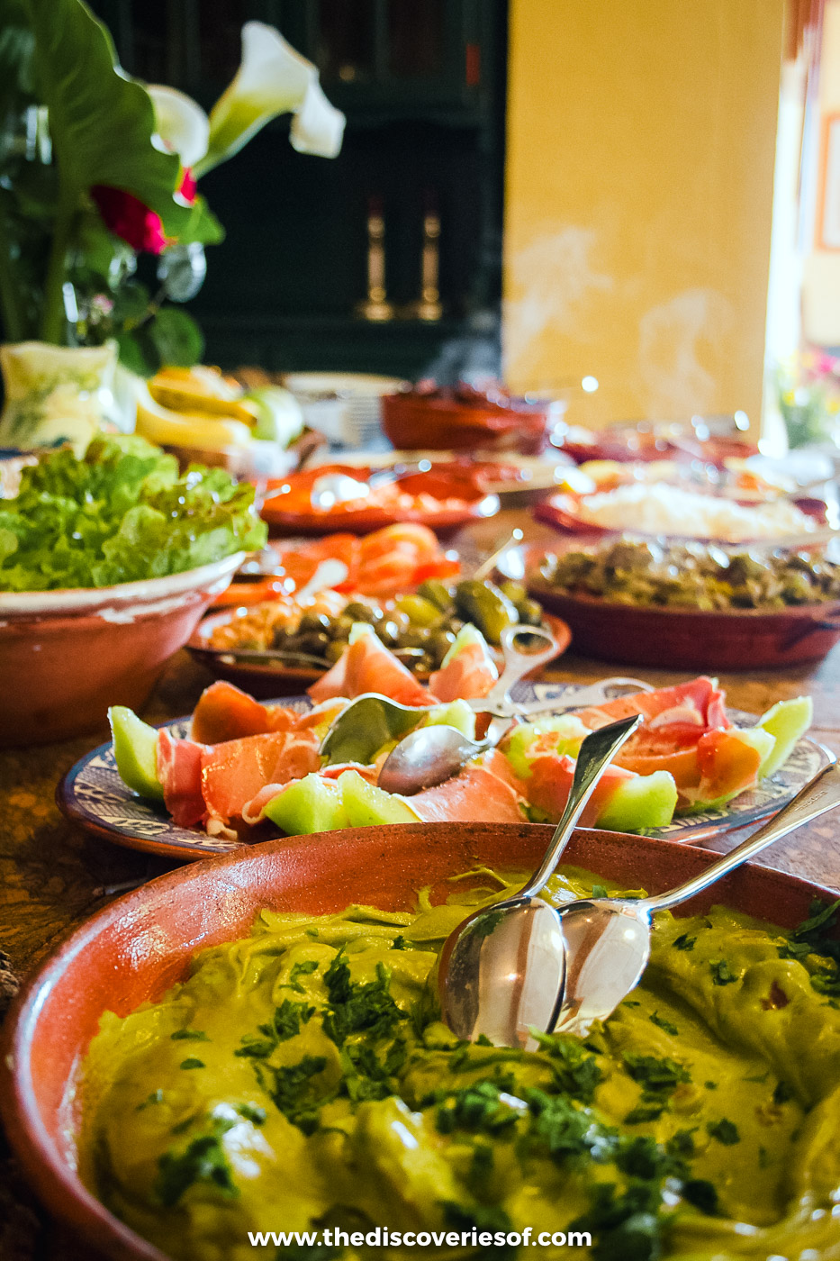 Bowls of salad, olives, melon with cured ham and a herb-topped dish laid out on a long table at Quinta do Barranco da Estrada