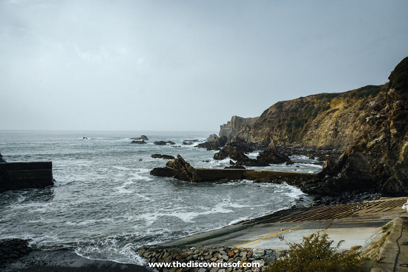 Grey Atlantic waves breaking over the rocks at the narrow harbour entrance of Azenha do Mar on the Alentejo coast