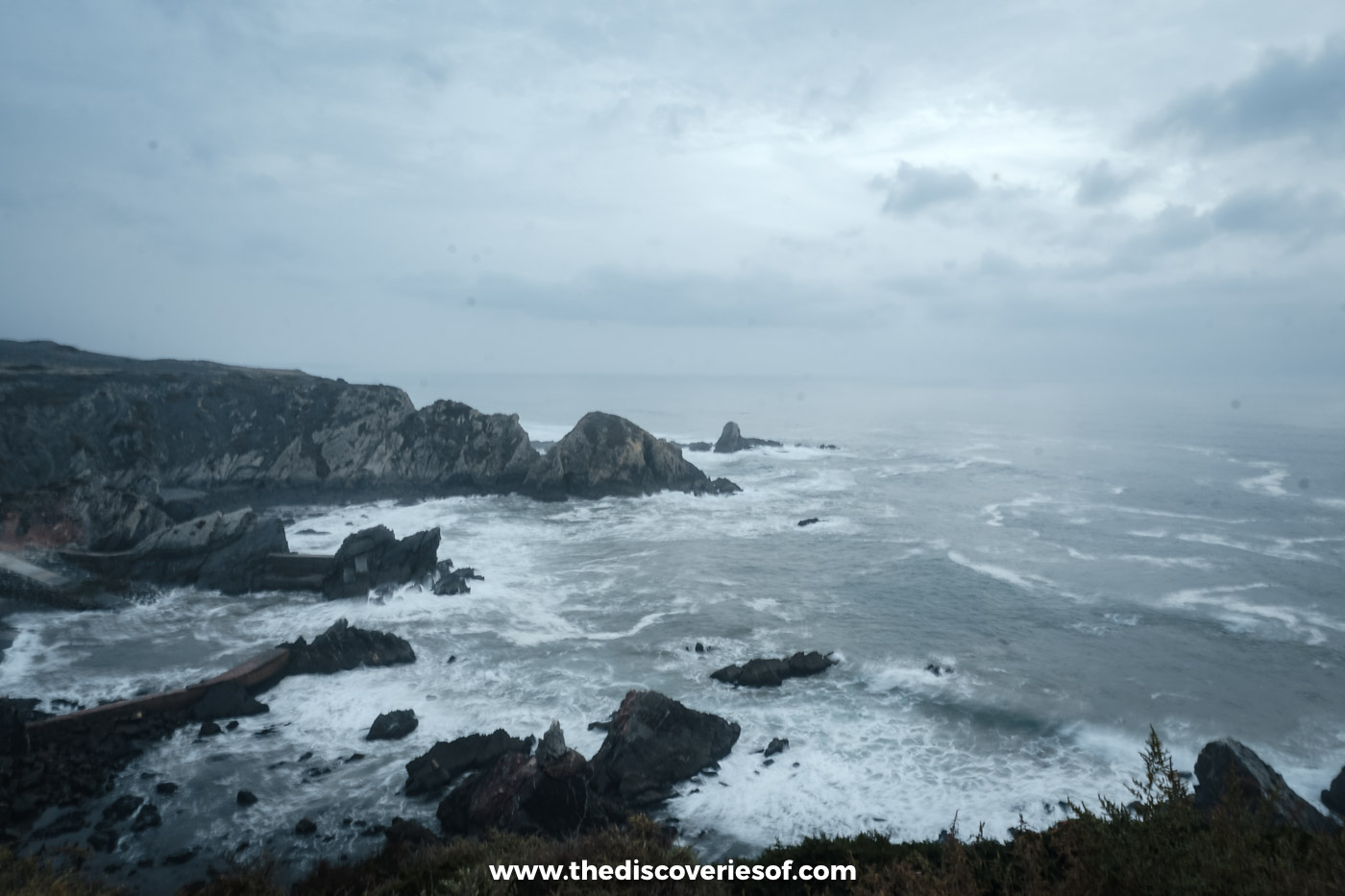 Grey October clouds over dark rocky headlands, sea stacks and white surf on the Atlantic coast north of Odeceixe