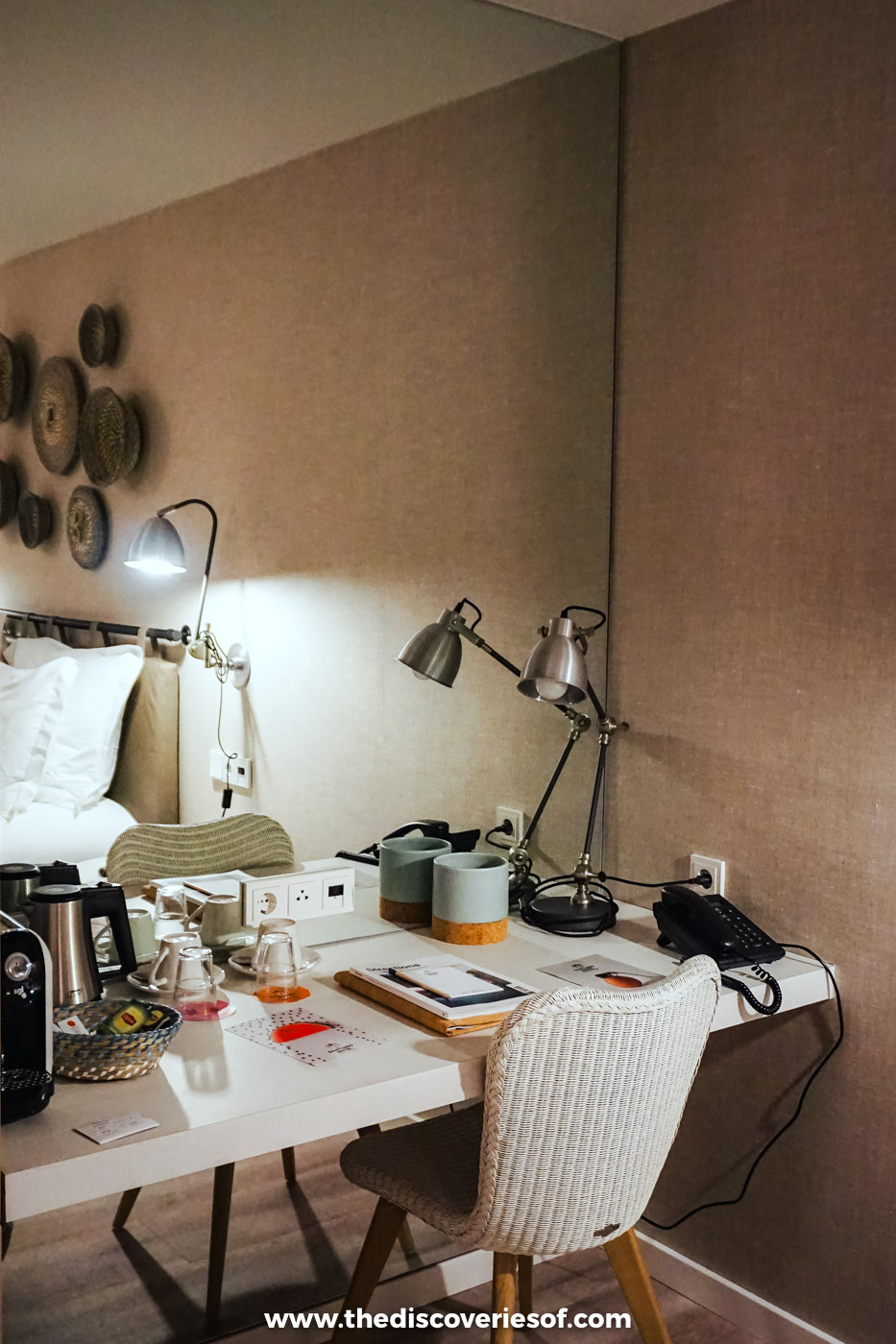A hotel bedroom desk with lamps, a woven chair and woven baskets hung on the wall at Octant Santiago in Santiago do Cacém