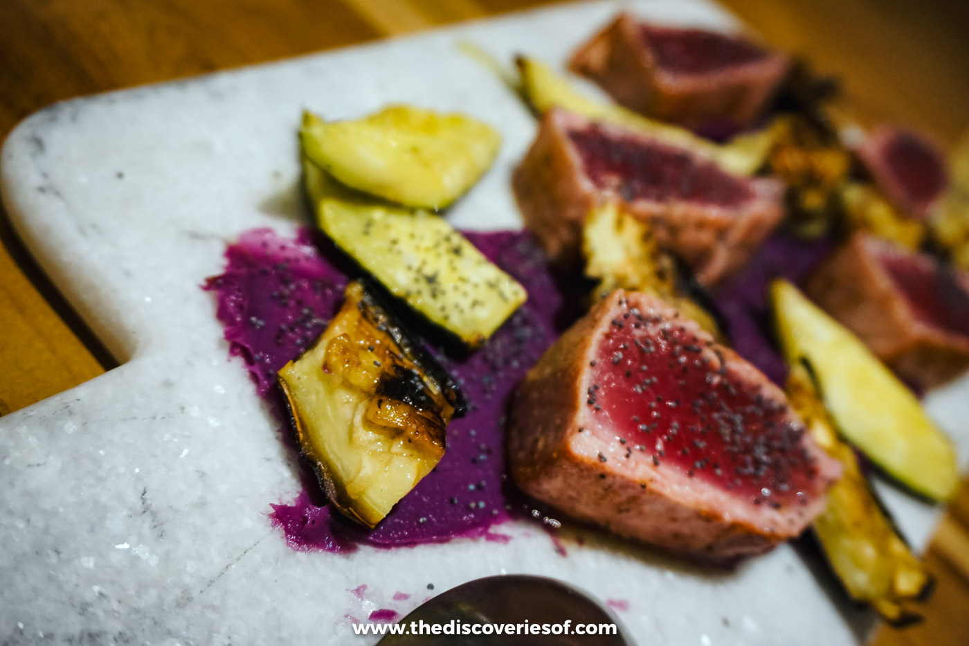 Slices of seared tuna with roasted sweet potato and a purple purée on a white marble board in Santiago do Cacém