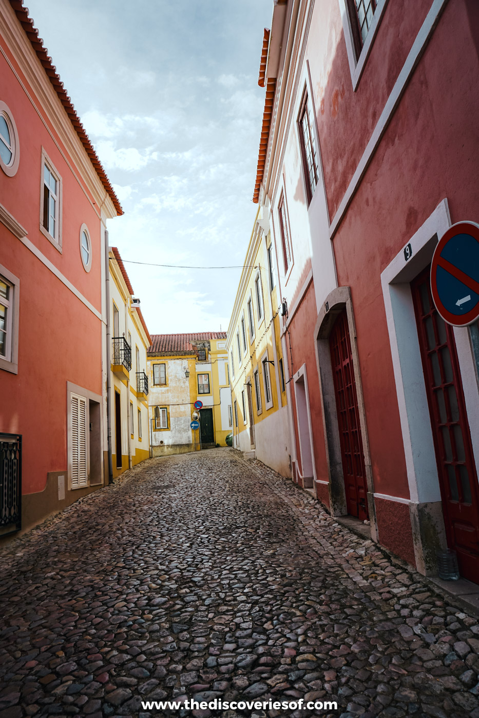 A cobbled street lined with red, pink and yellow houses in Santiago do Cacém, the start of the Historical Way
