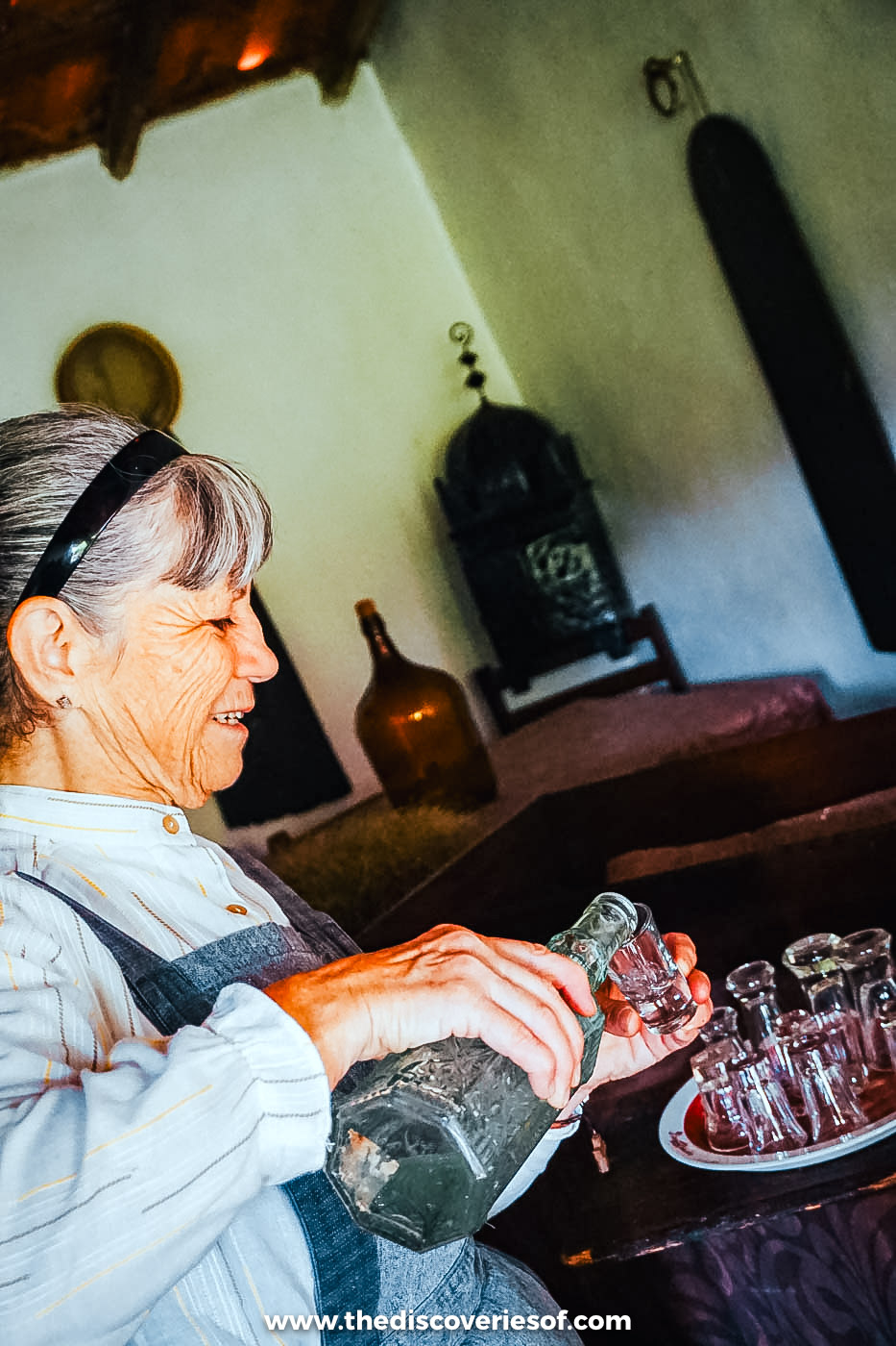 Odete pouring medronho from a glass bottle into small glasses in her farmhouse in Santa Clara-a-Velha