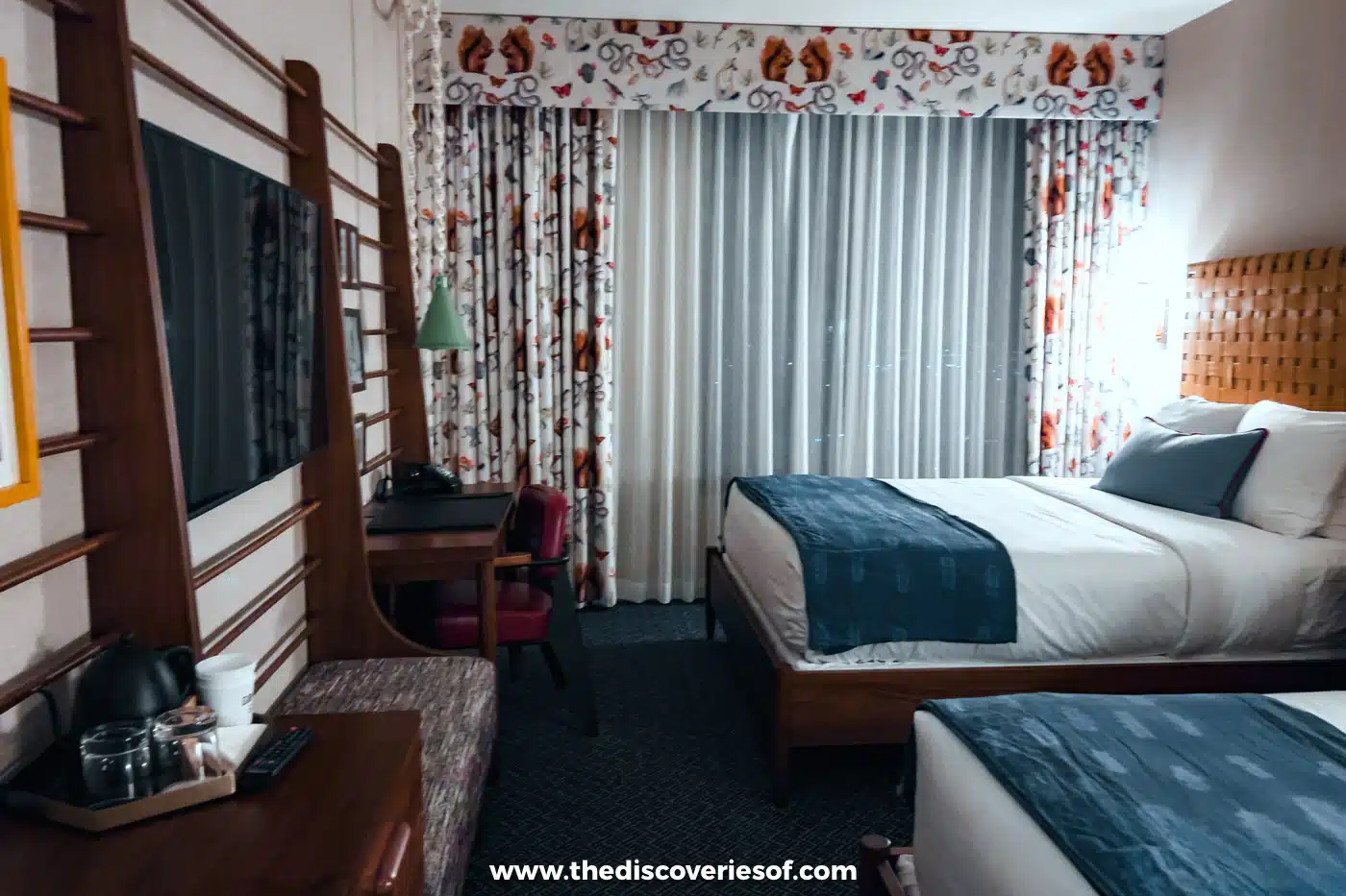 Two beds, patterned curtains and retro wooden furniture in a room at the Graduate by Hilton Tucson