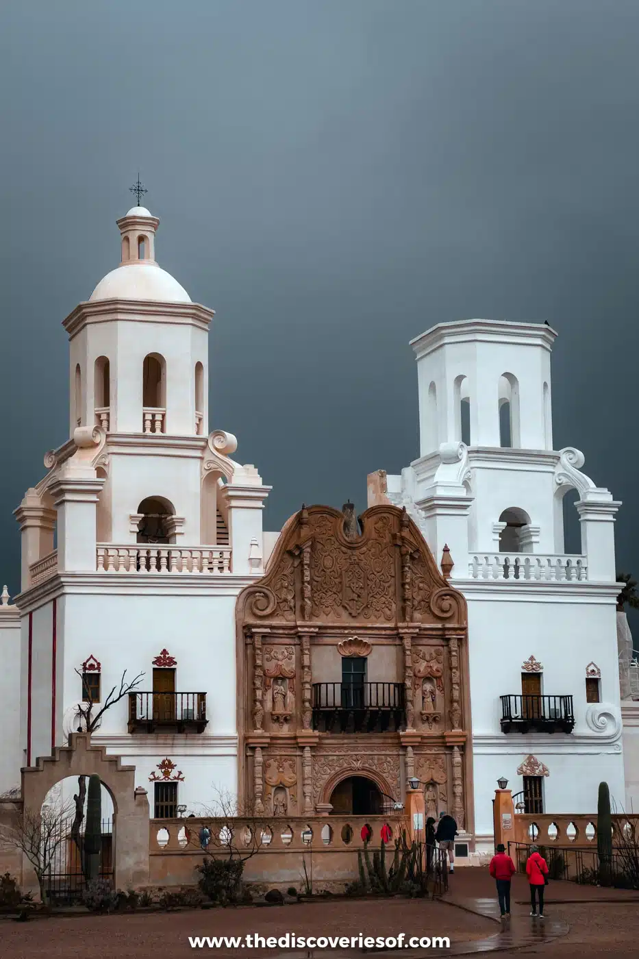The white towers and carved façade of Mission San Xavier del Bac under a dark winter sky near Tucson