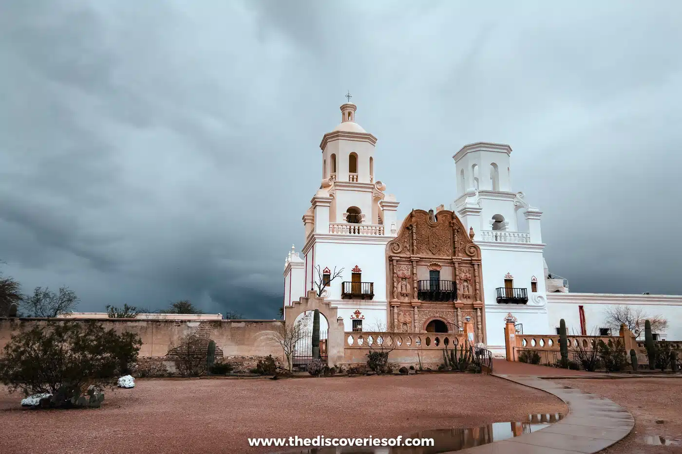 Mission San Xavier del Bac and its puddled plaza beneath grey storm clouds south of Tucson, Arizona
