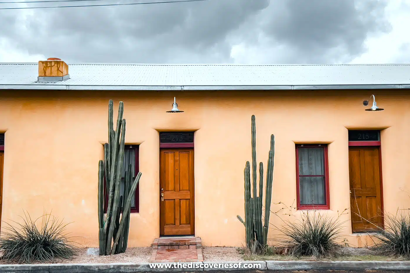 A yellow adobe house with wooden doors and tall cacti on a street in Barrio Viejo, Tucson
