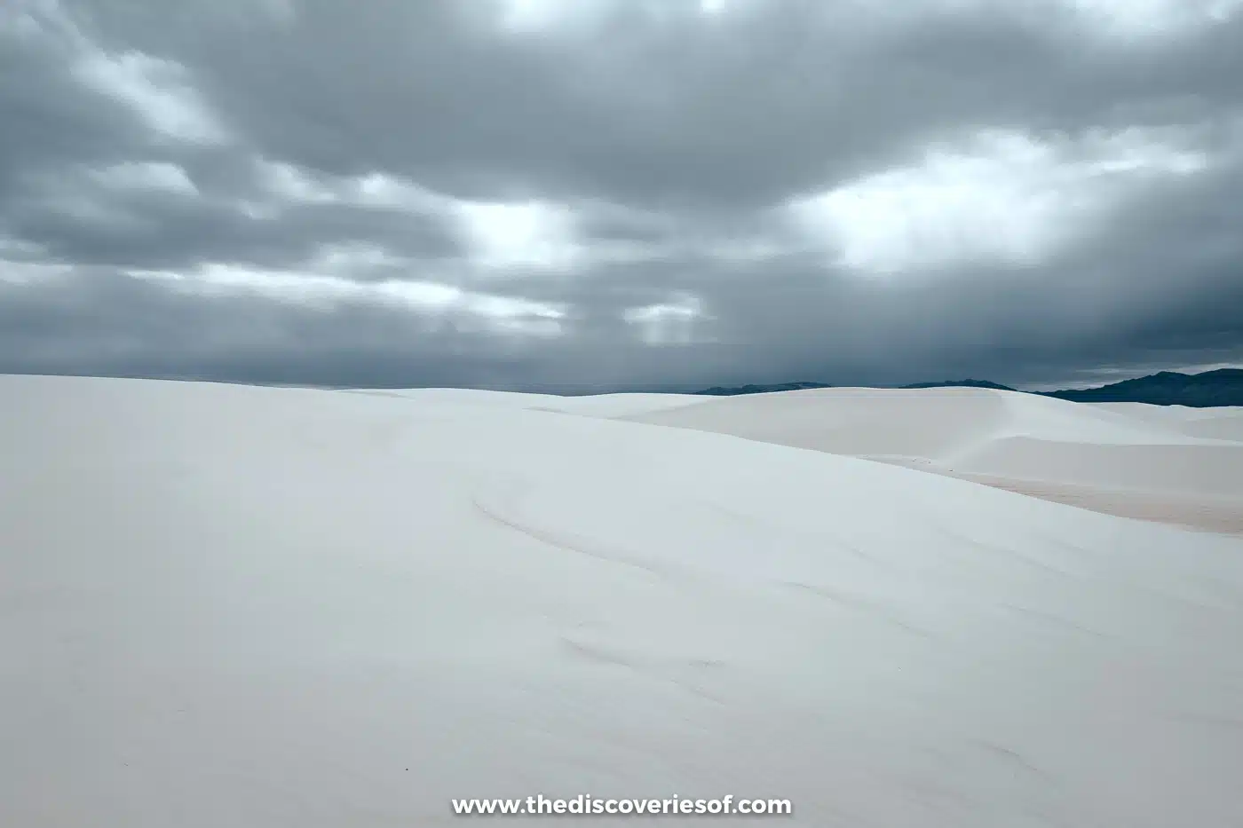 Smooth white gypsum dunes under heavy grey winter clouds at White Sands National Park