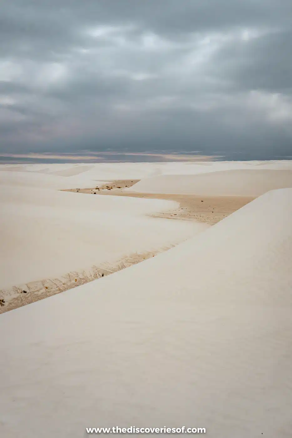 Rippled white gypsum dunes stretching towards distant mountains under a cloudy sky at White Sands