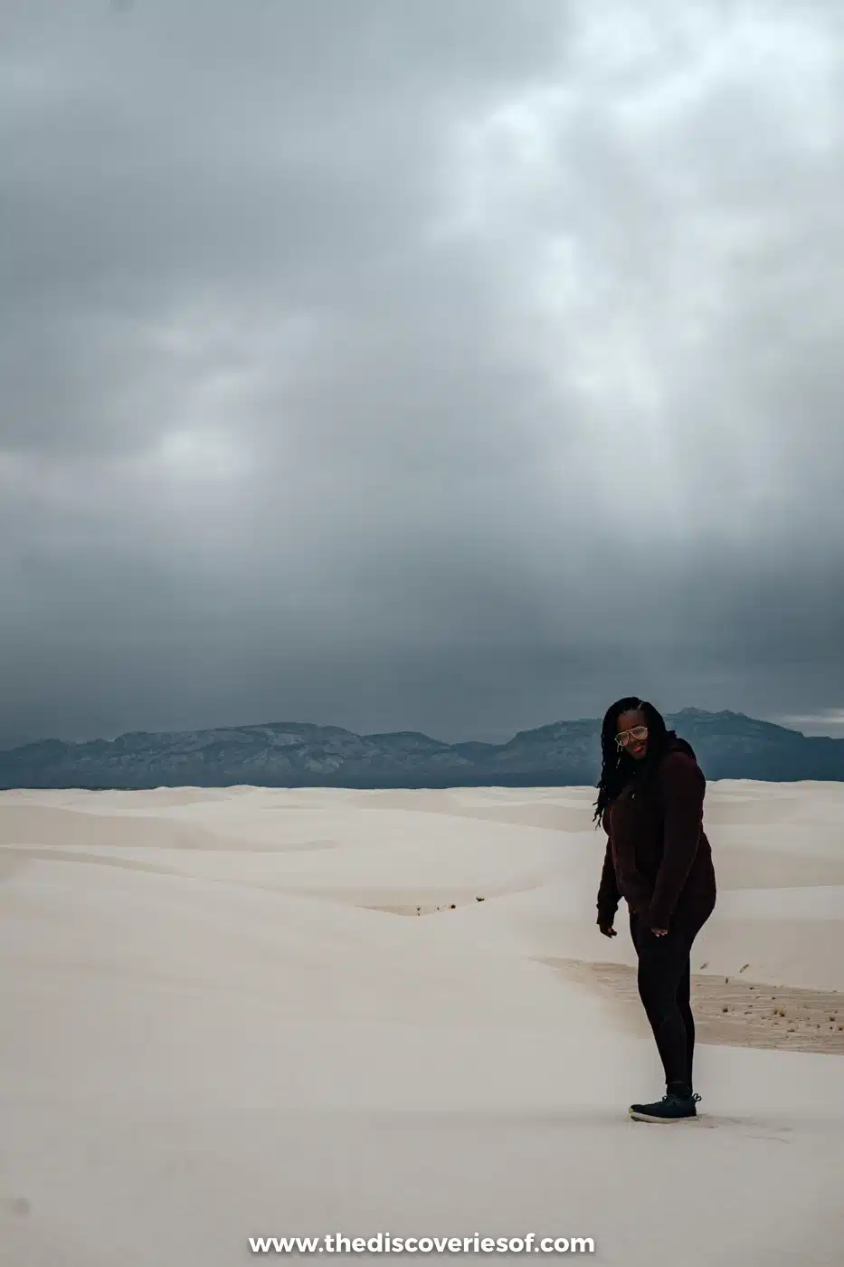 Julianna standing on the white gypsum dunes of White Sands National Park under dark February rain clouds